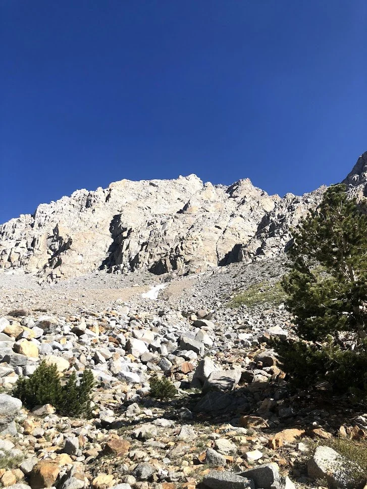 A rocky mountain landscape with large boulders and sparse vegetation under a clear blue sky.