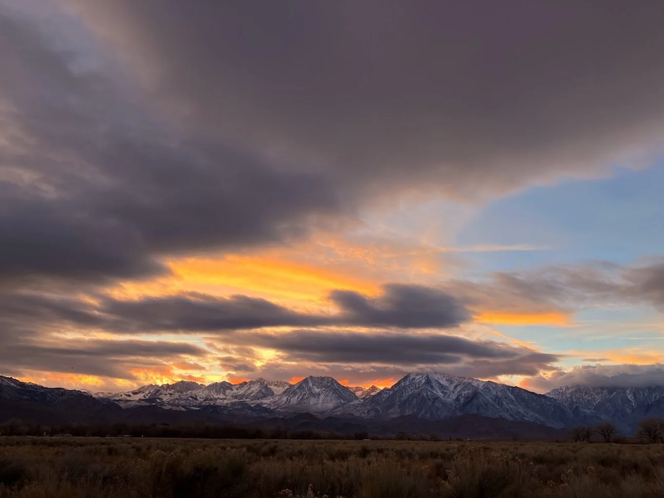 Sunset over snow-capped mountains with dark clouds and orange sky at dusk