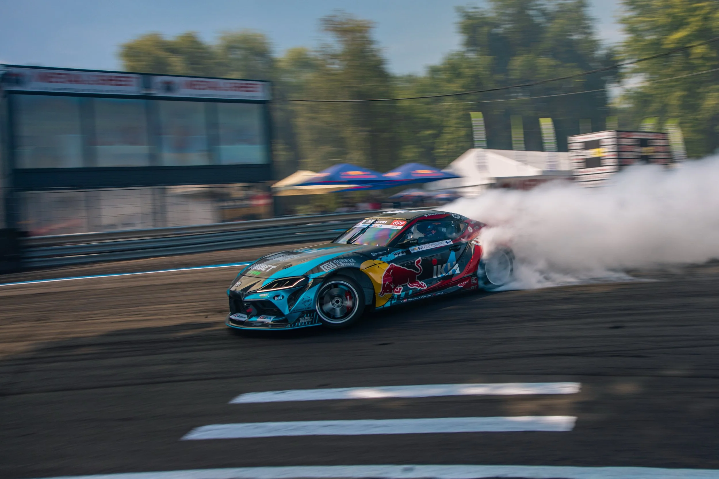 A race car with Red Bull branding skidding on a track, creating smoke behind it during a race.