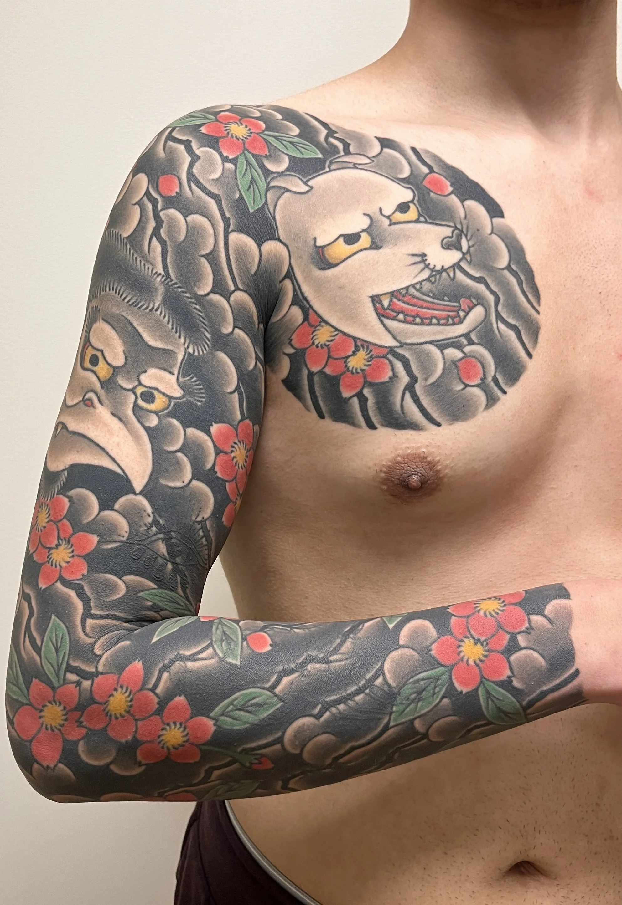 A man with traditional Japanese style tattoos on his chest, arm, and shoulder featuring a fierce depicted animal, possibly a cat or tiger, with red flowers and black leaves surrounding the designs.