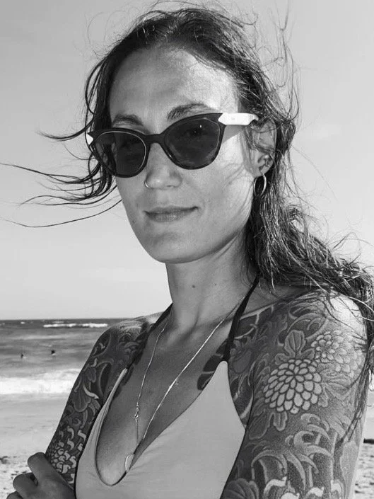 Woman with tattoos, wearing sunglasses, at the beach in black and white.