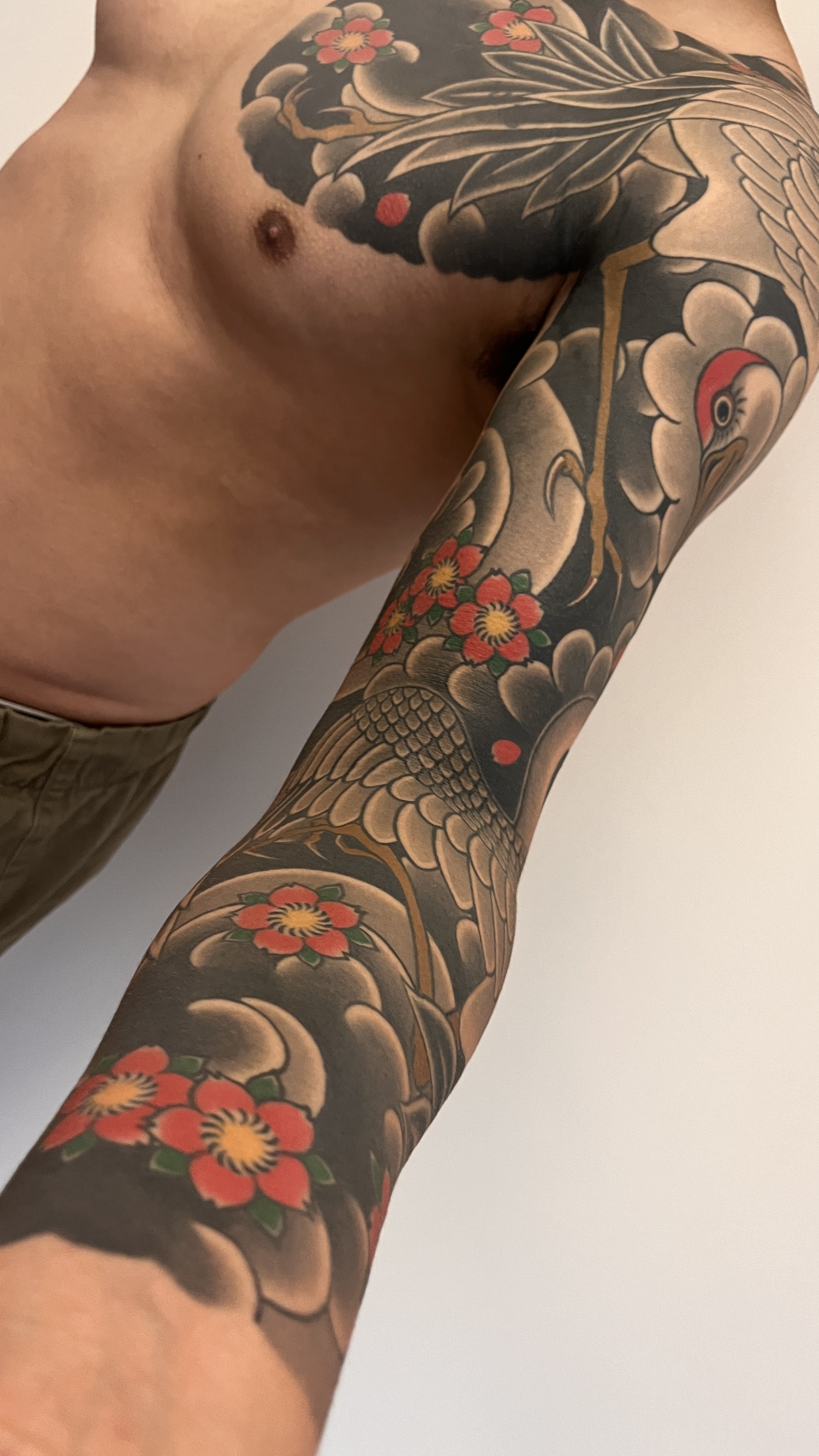 Close-up of a person's arm and shoulder with traditional-style Japanese tattoo featuring a crane, cherry blossoms, and waves.