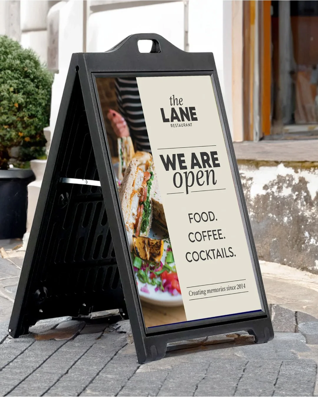 A sidewalk sandwich board sign outside a restaurant announcing that the restaurant, The Lane, is open for food, coffee, and cocktails.