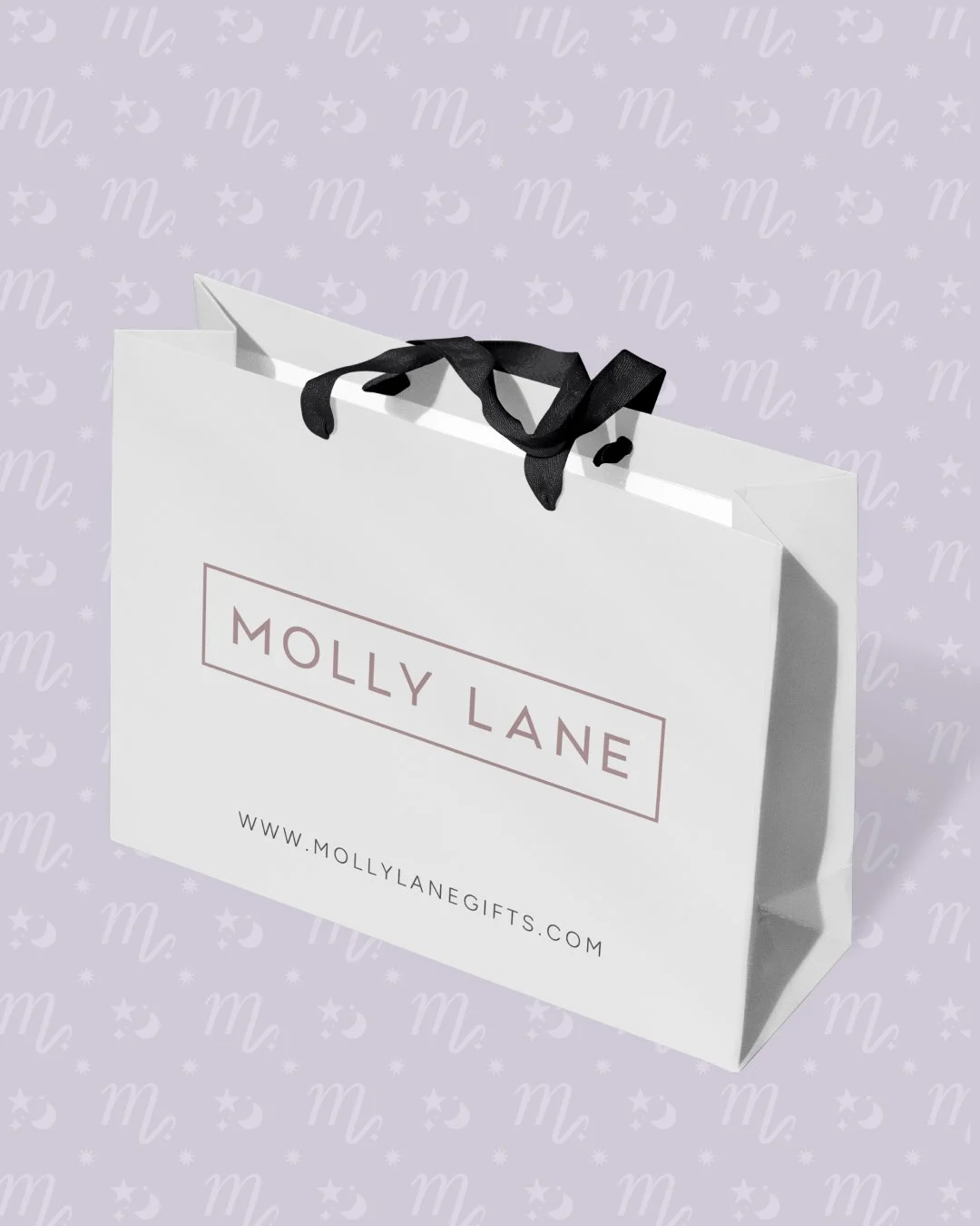 White shopping bag with black ribbon handles, labeled with "Molly Lane" and website "www.mollylanegifts.com" against a light purple background with a pattern of stars, moons, and the letter "m."