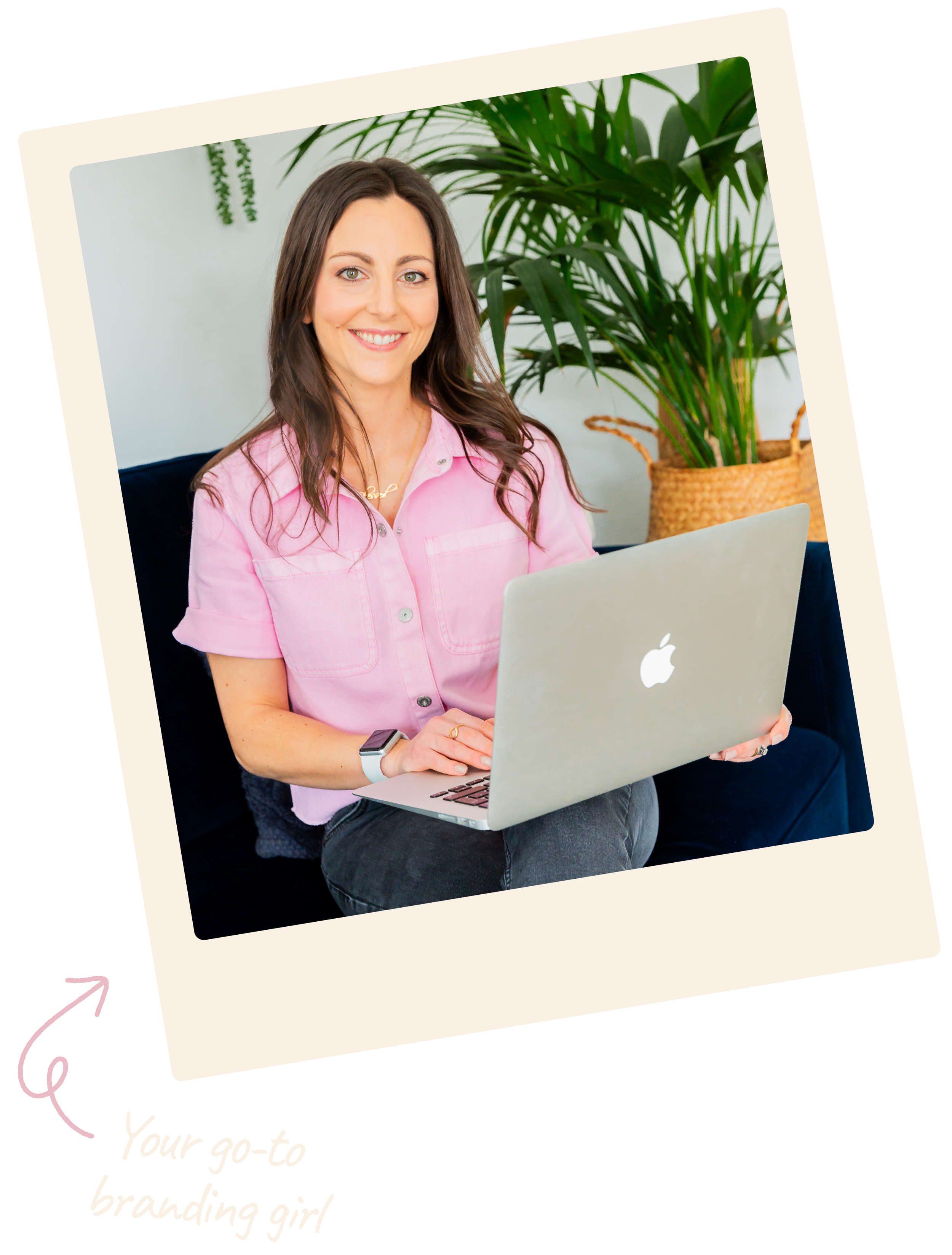 Lauren Armstrong, brand designer at Lauren's Design Studio. A woman with long brown hair, wearing a pink shirt, sitting on a black sofa, working on a silver MacBook laptop, with green plants in the background.