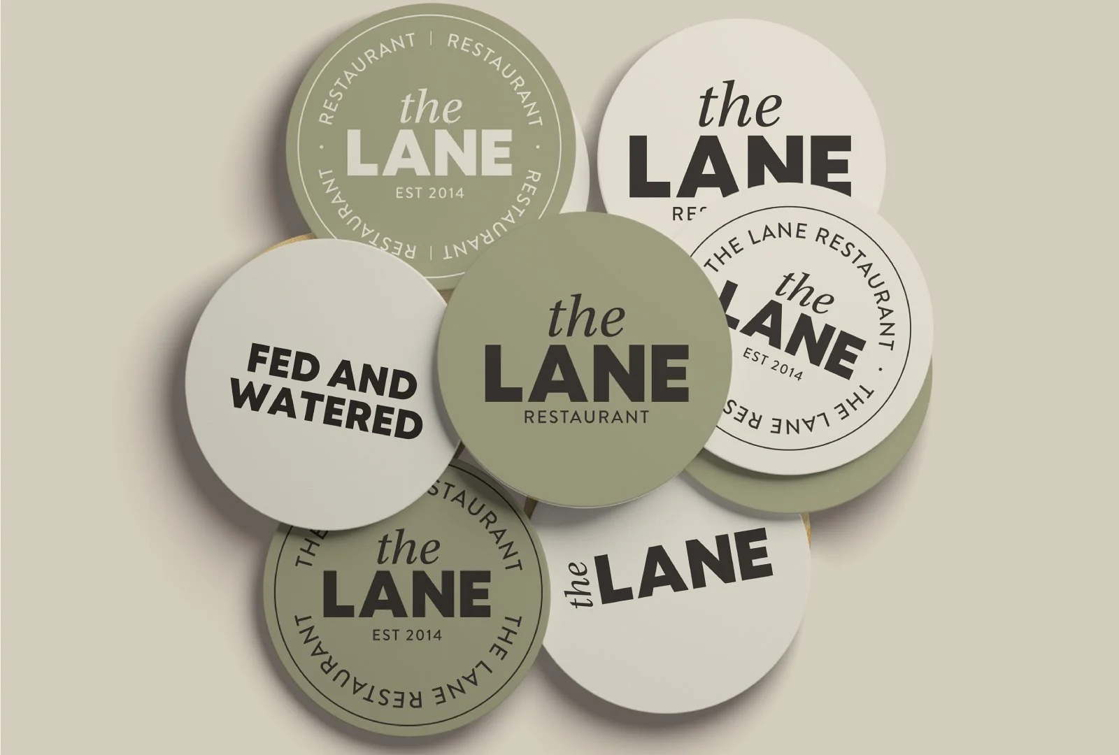 Collection of circular stickers with the logo of "The Lane" restaurant, showing different designs and colors including green and white, with variations of text like "EST 2014" and "Fed and Watered".