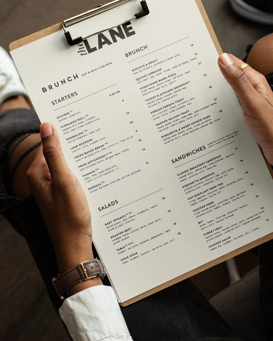 A person holding a menu at a restaurant, showing food options for brunch and sandwiches.