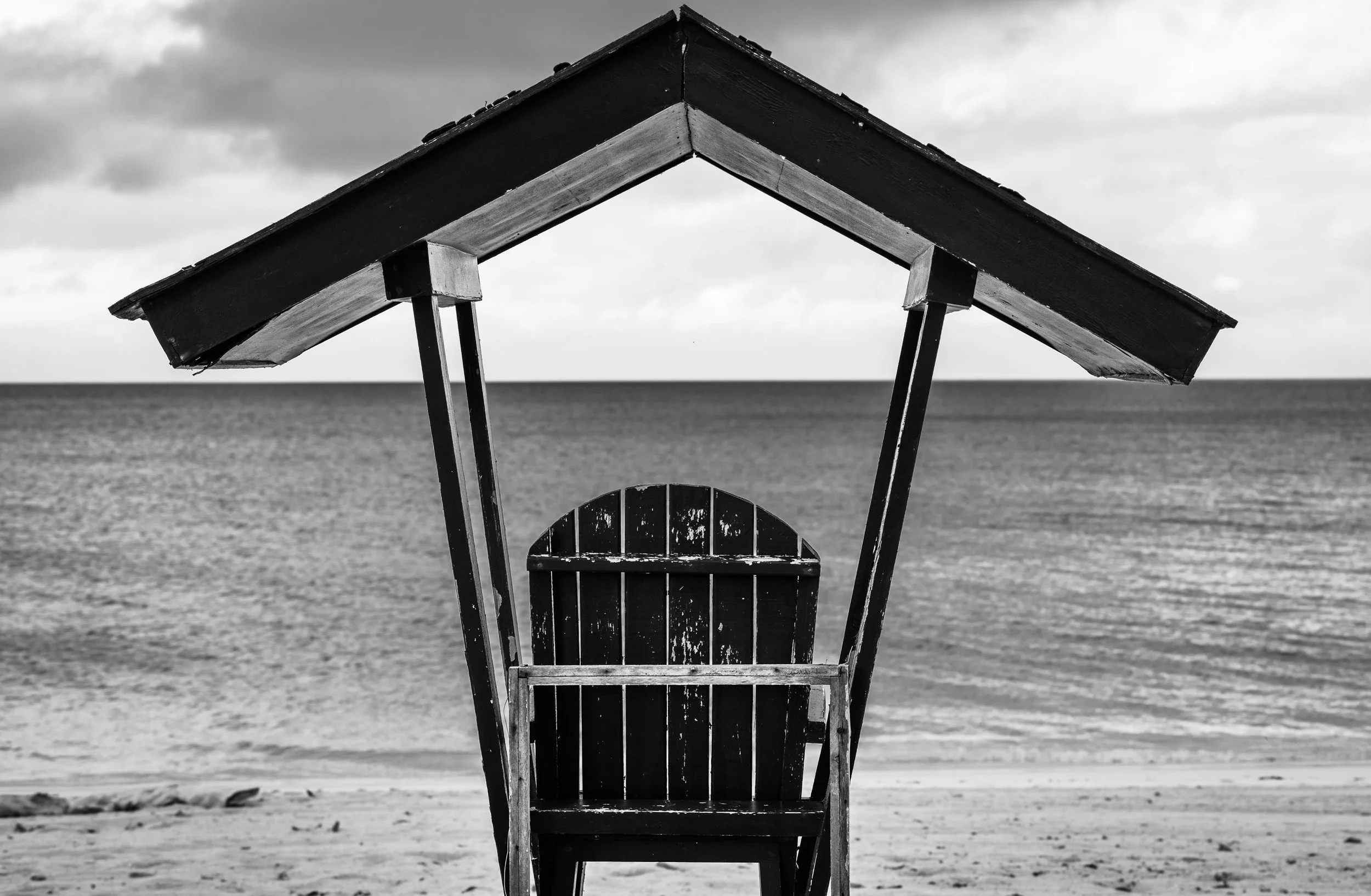 Black and white photo of a lifeguard chair on a beach, facing the ocean.