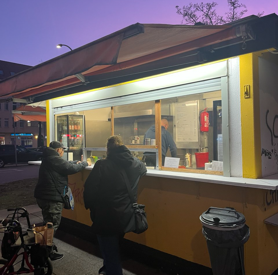 People ordering food at a small outdoor food stand during twilight.