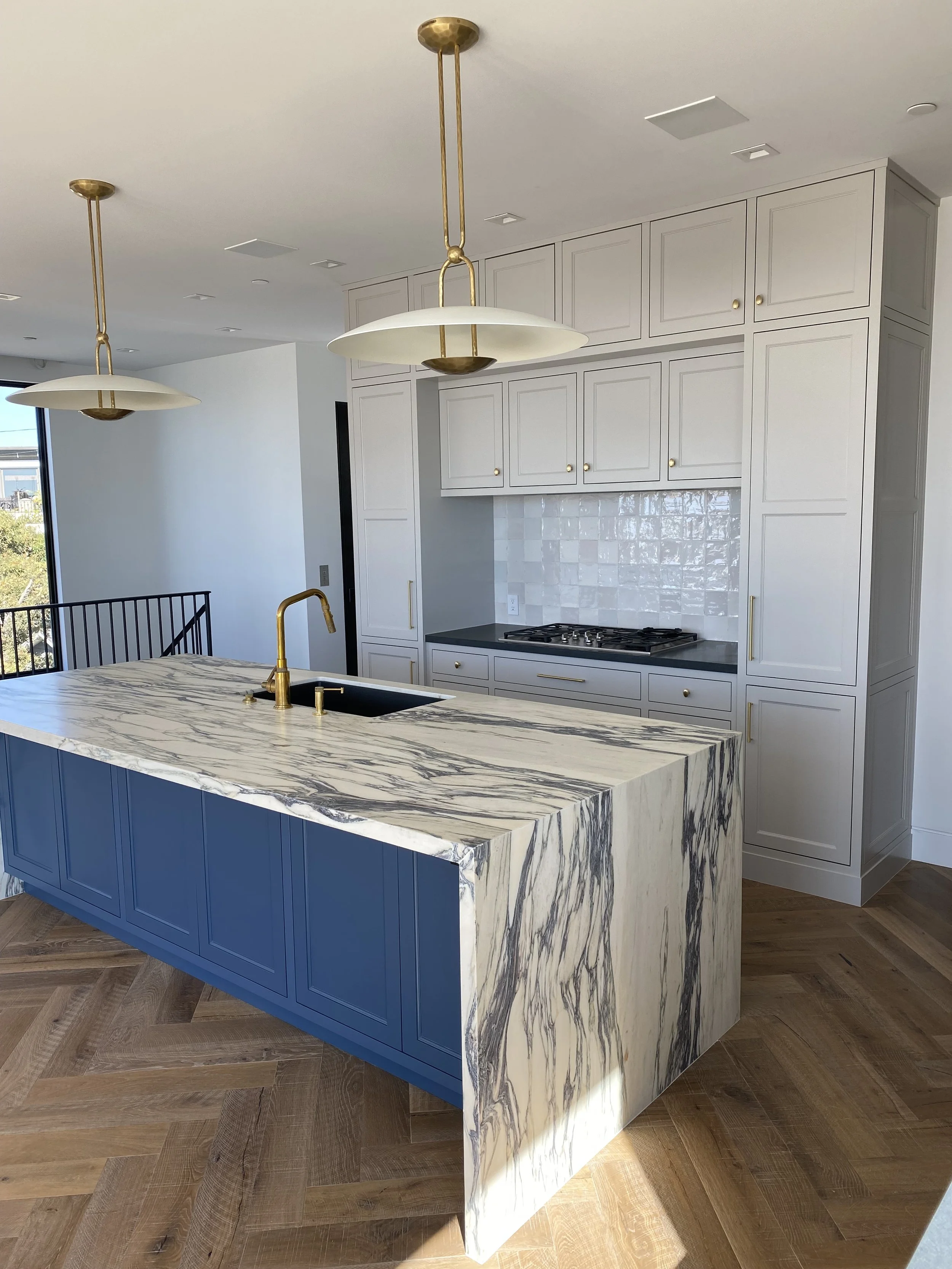 Modern kitchen with a marble island, white cabinets, and brass fixtures.