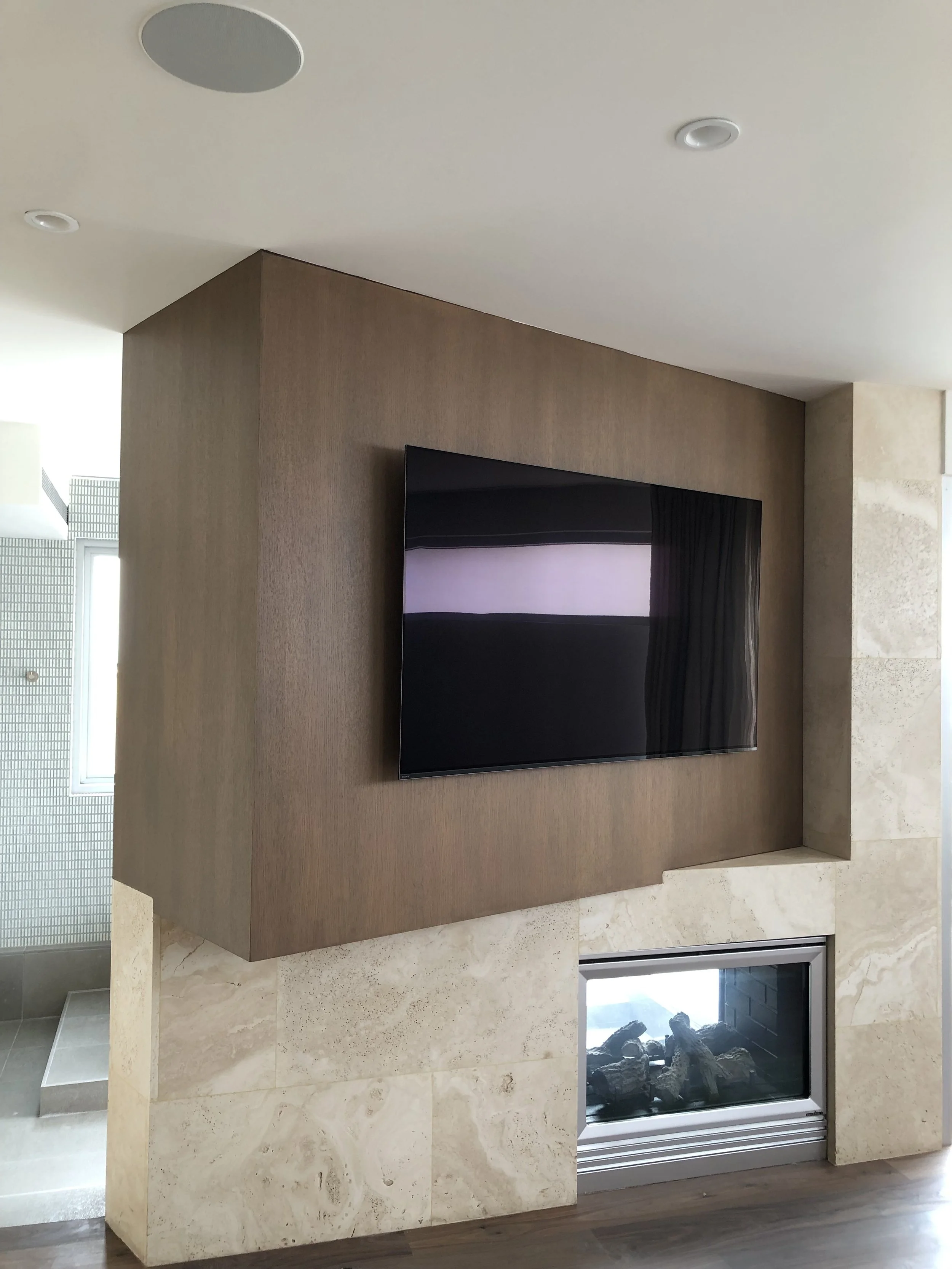 Modern living room with a wall-mounted flat-screen TV above a modern fireplace with rocks inside.