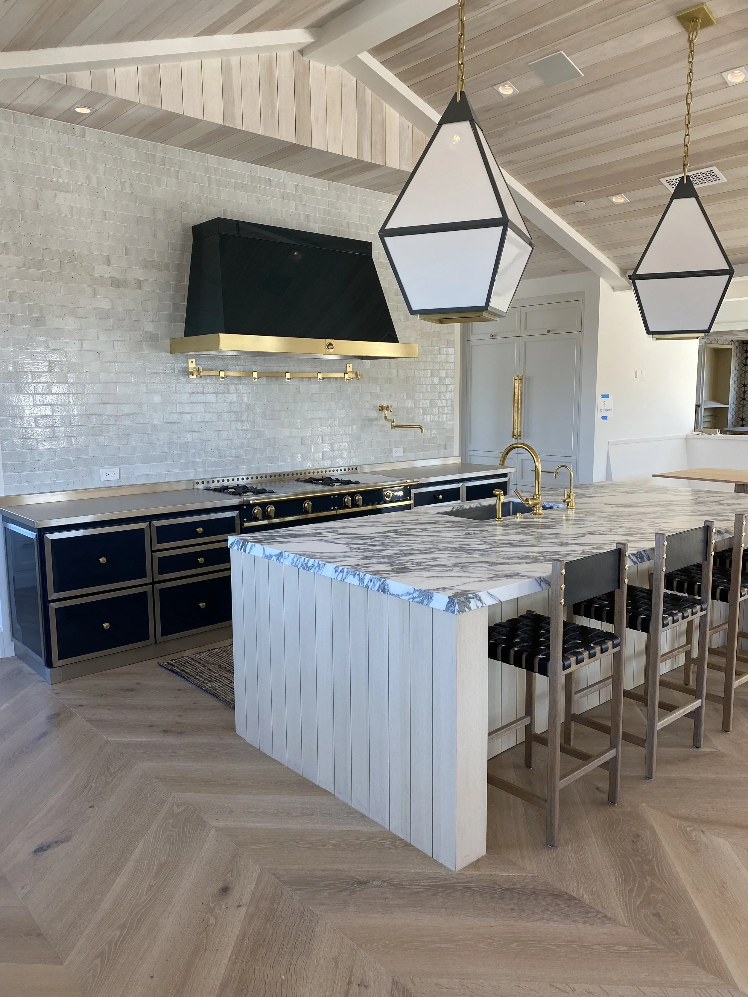 Modern kitchen with a white marble island, black and gold cabinetry, black range hood, and geometric pendant lights.