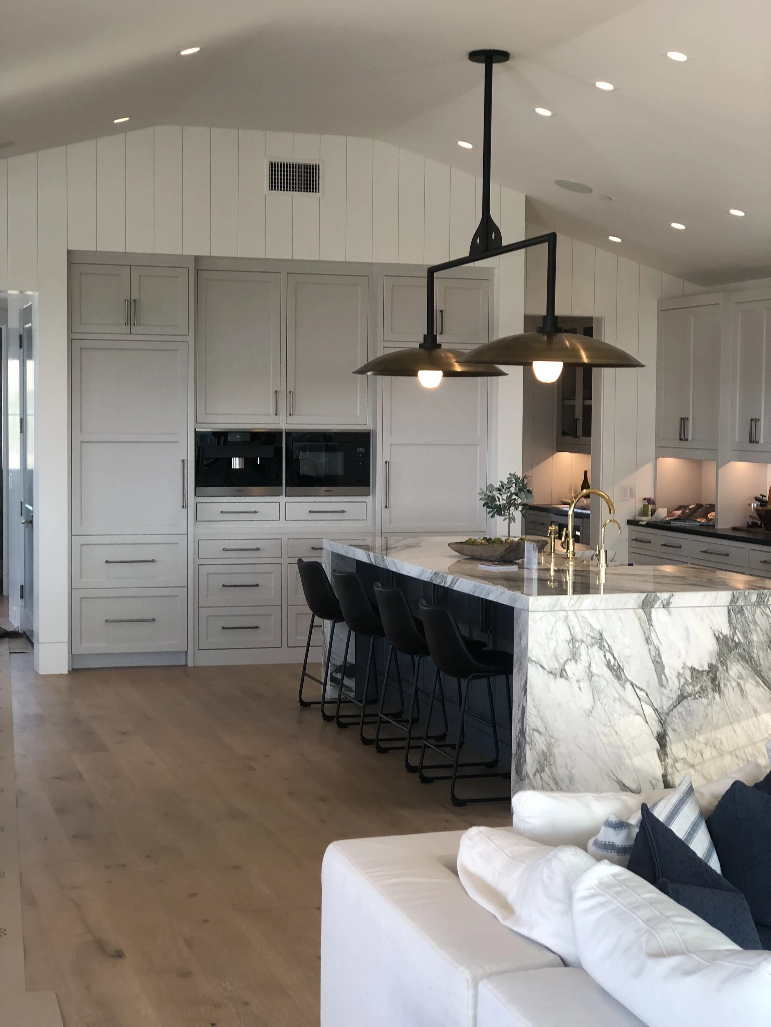 Modern kitchen with white cabinetry, a marble island with a gold faucet, black bar stools, and black pendant lighting, in an open-concept living space.