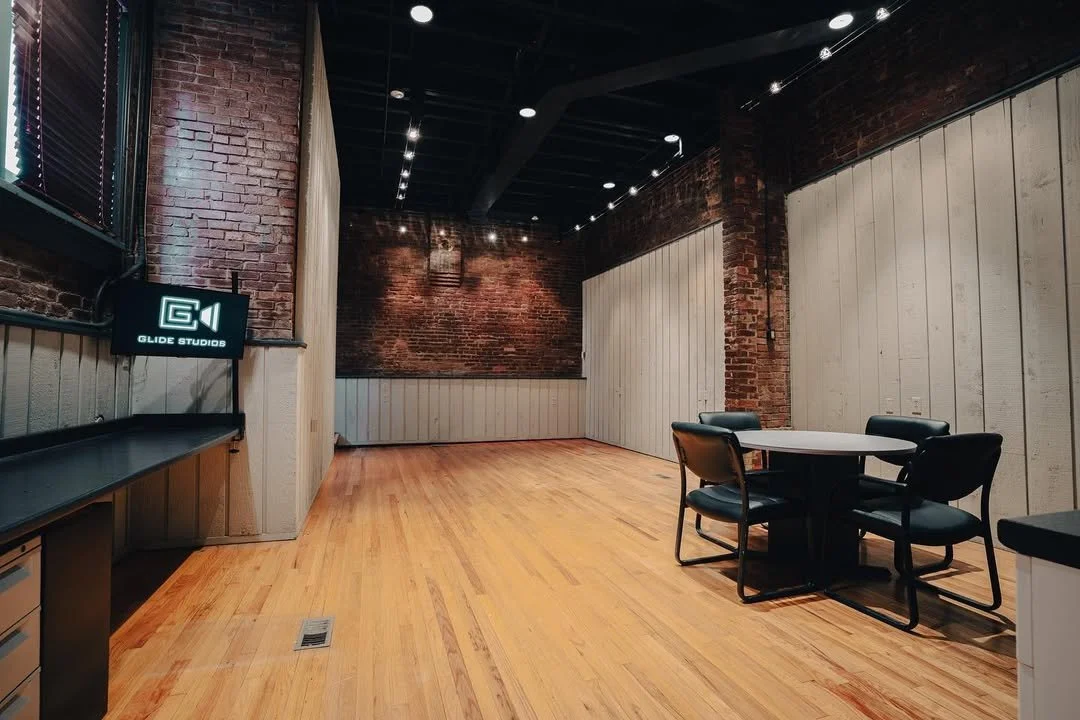 Empty room with wooden flooring, brick walls, a round table with four chairs, and a wall-mounted screen with the logo 'G1 Glide Studios'.
