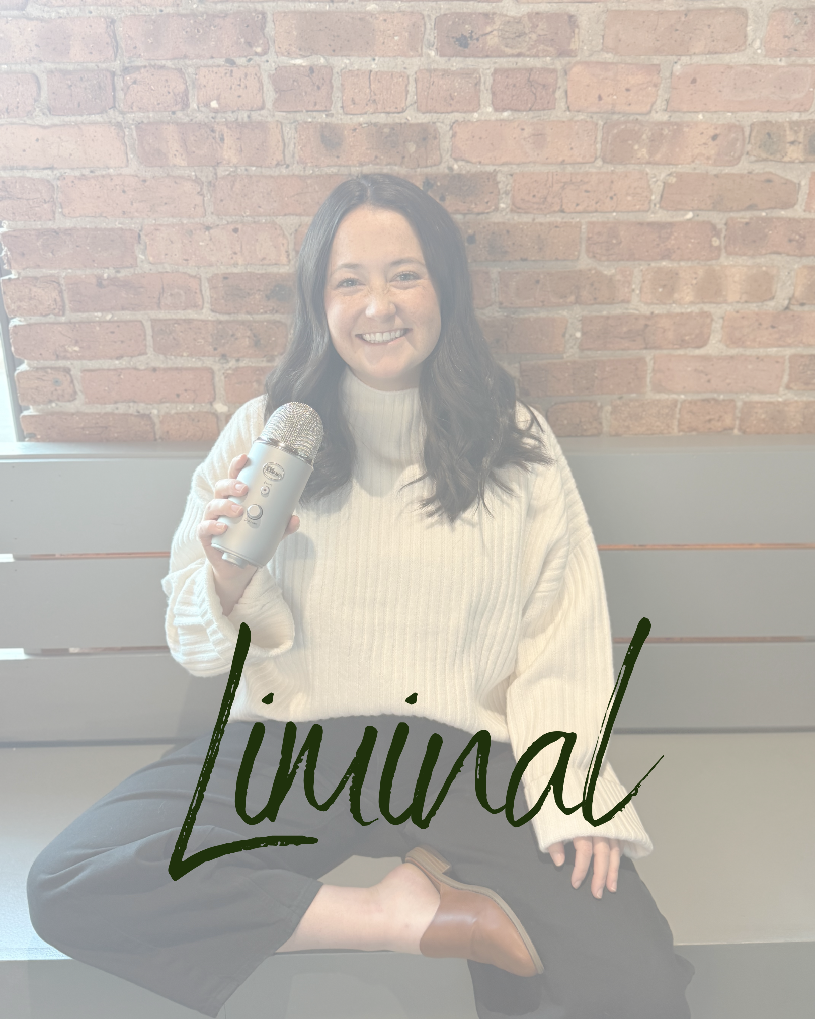 A woman with long dark hair, wearing a cream-colored sweater, sitting cross-legged on the floor with a brick wall background, holding a microphone, and smiling. The word 'Liwali' is written over her in stylized green script.