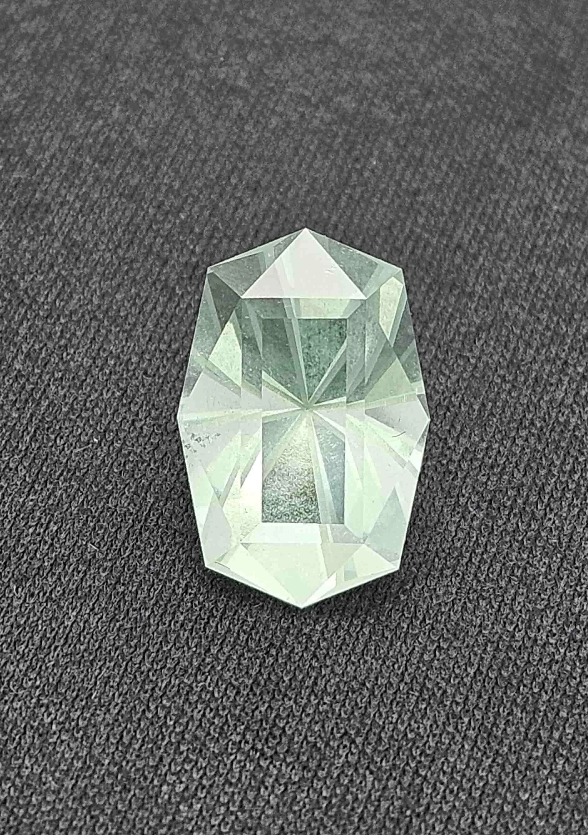 A large, transparent, multifaceted crystal placed on a black textured surface.