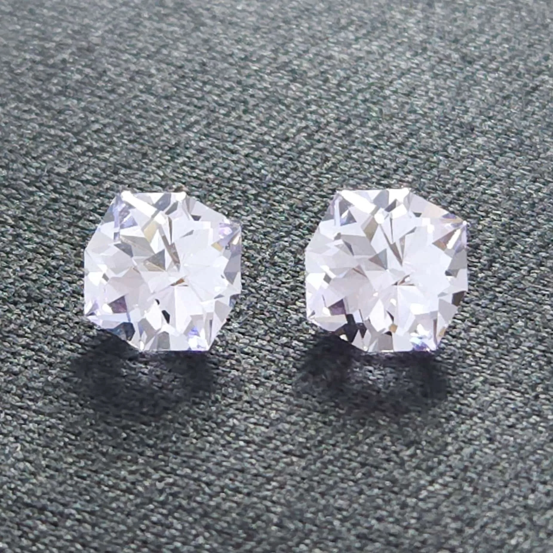 Two large, faceted clear jewels, possibly diamonds or crystals, are placed on a gravel surface with shadows cast nearby.