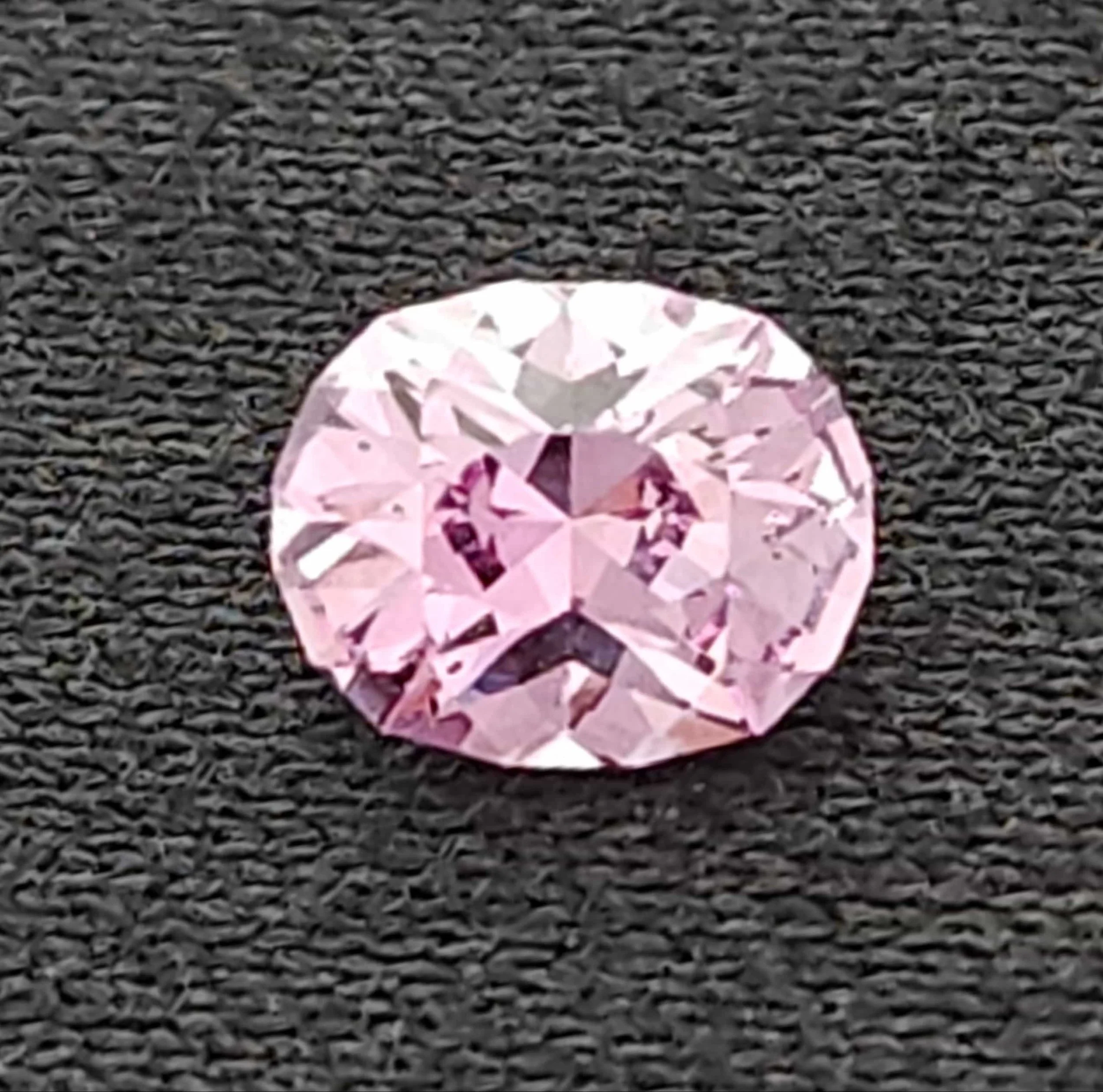 A pink, round, faceted Montana Sapphire gemstone on a black textured surface.