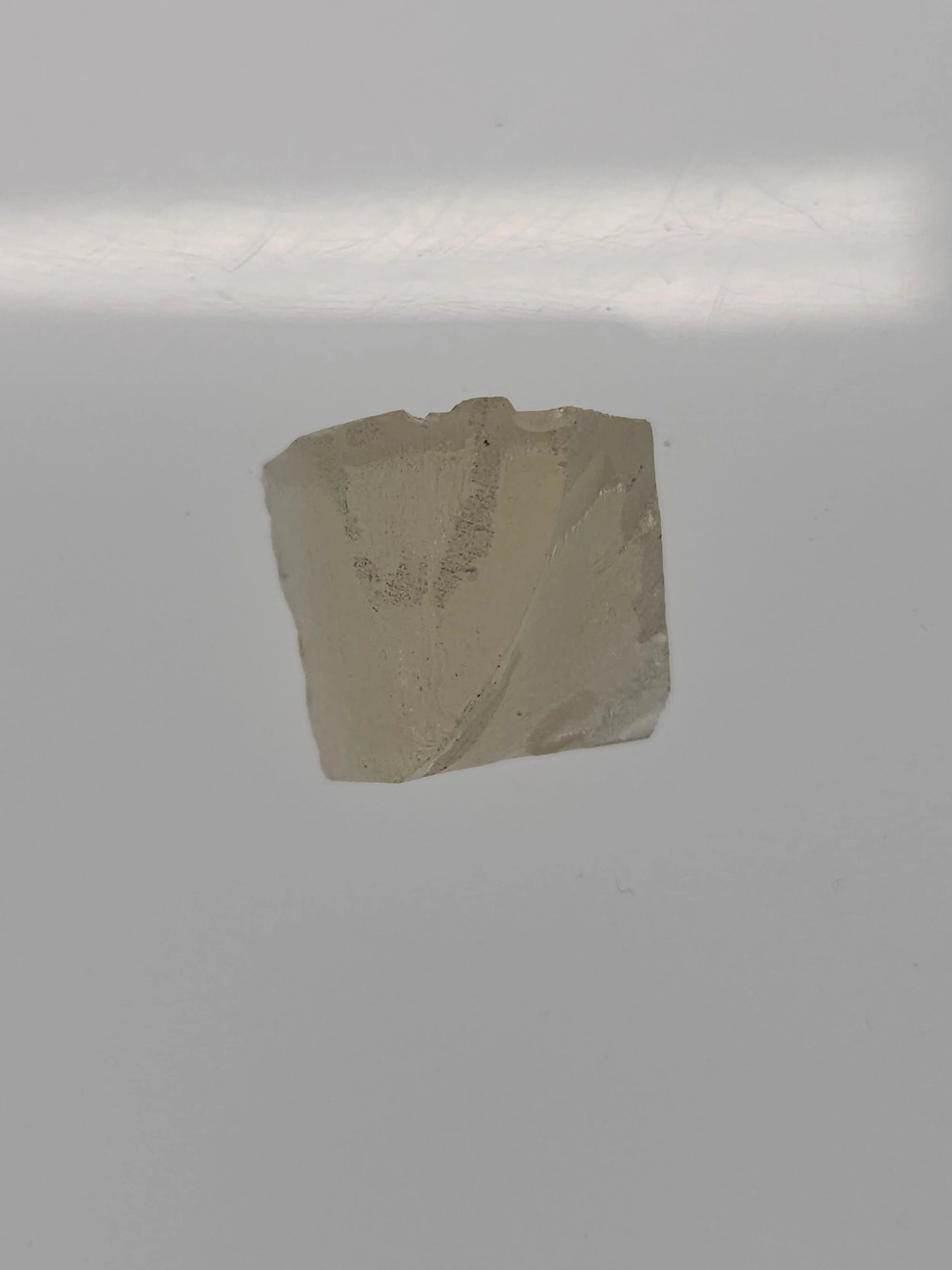 A small, irregularly shaped, white or translucent mineral or rock on a plain white surface.