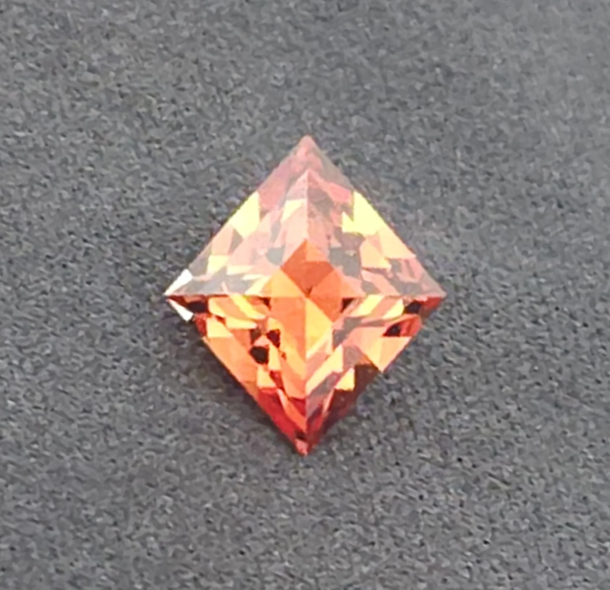 Close-up of a colorful reflective object with a diamond pattern, resting on a textured gray surface.
