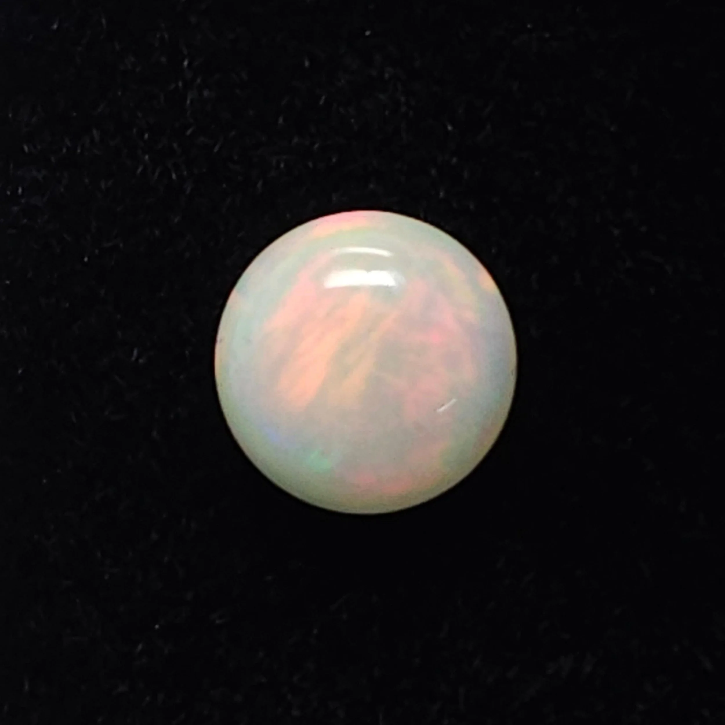 Close-up of a pearl with colorful iridescence on a dark surface.