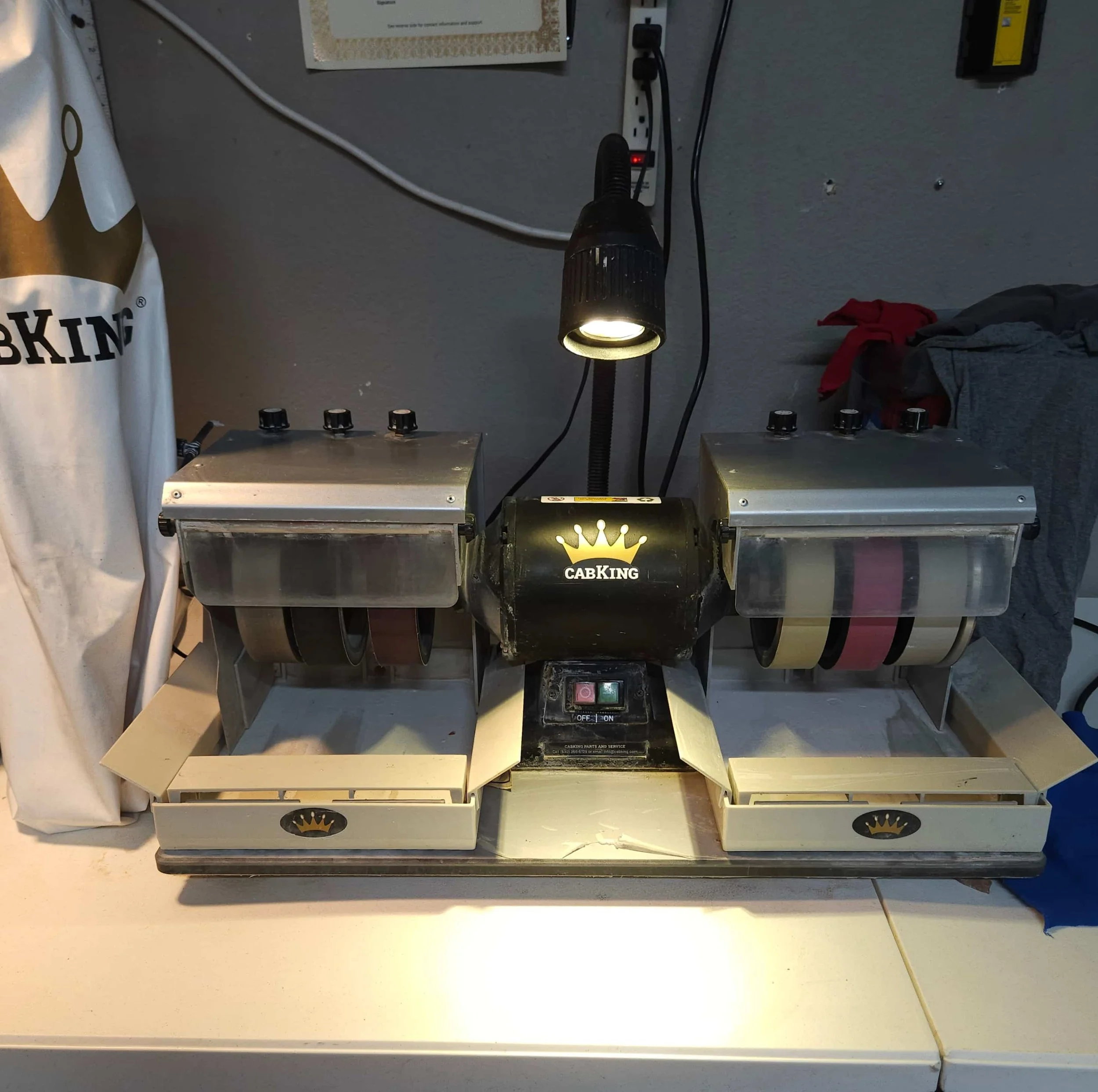 Close-up of a workbench with a packaged product labeled 'CABKING' and a small lamp overhead illuminating the workspace, with electrical outlets and cords attached to the wall in the background.
