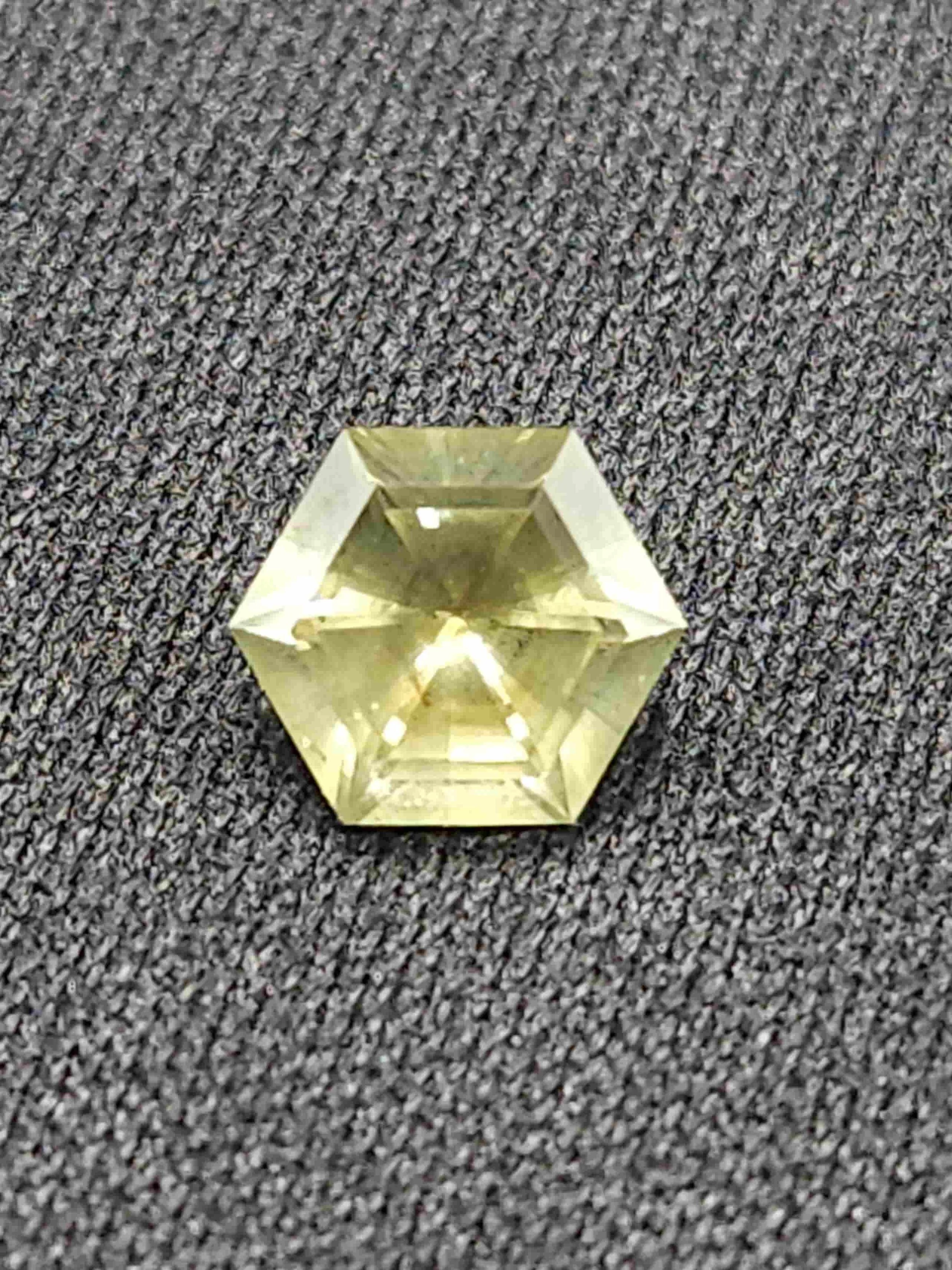 A small, clear, geometrically cut Montana sapphire resting on a textured gray surface.