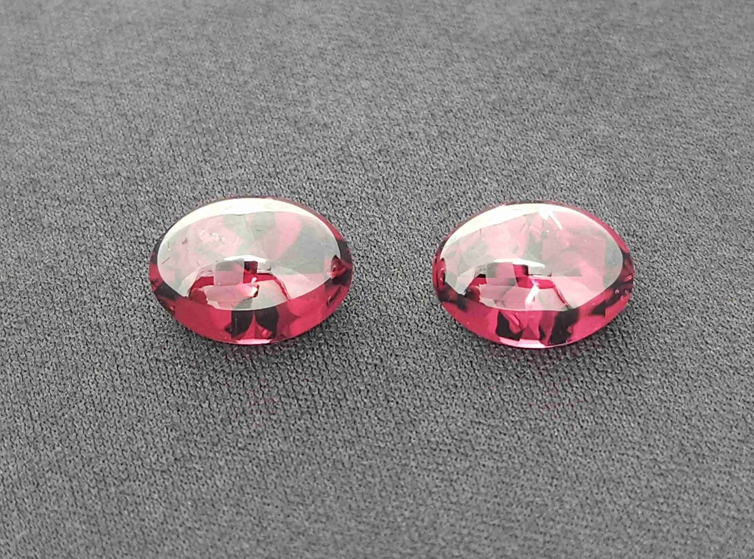 Two pink and clear glass marbles with black and pink patterns, placed on a textured gray surface.