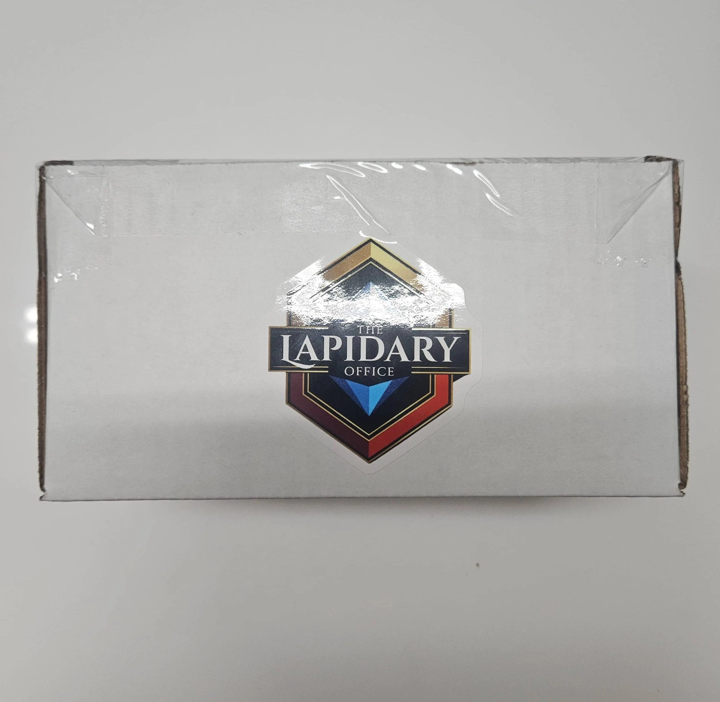 Close-up of a glass award with a black and gold emblem that says "The LAPIDARY Office" on a white surface.