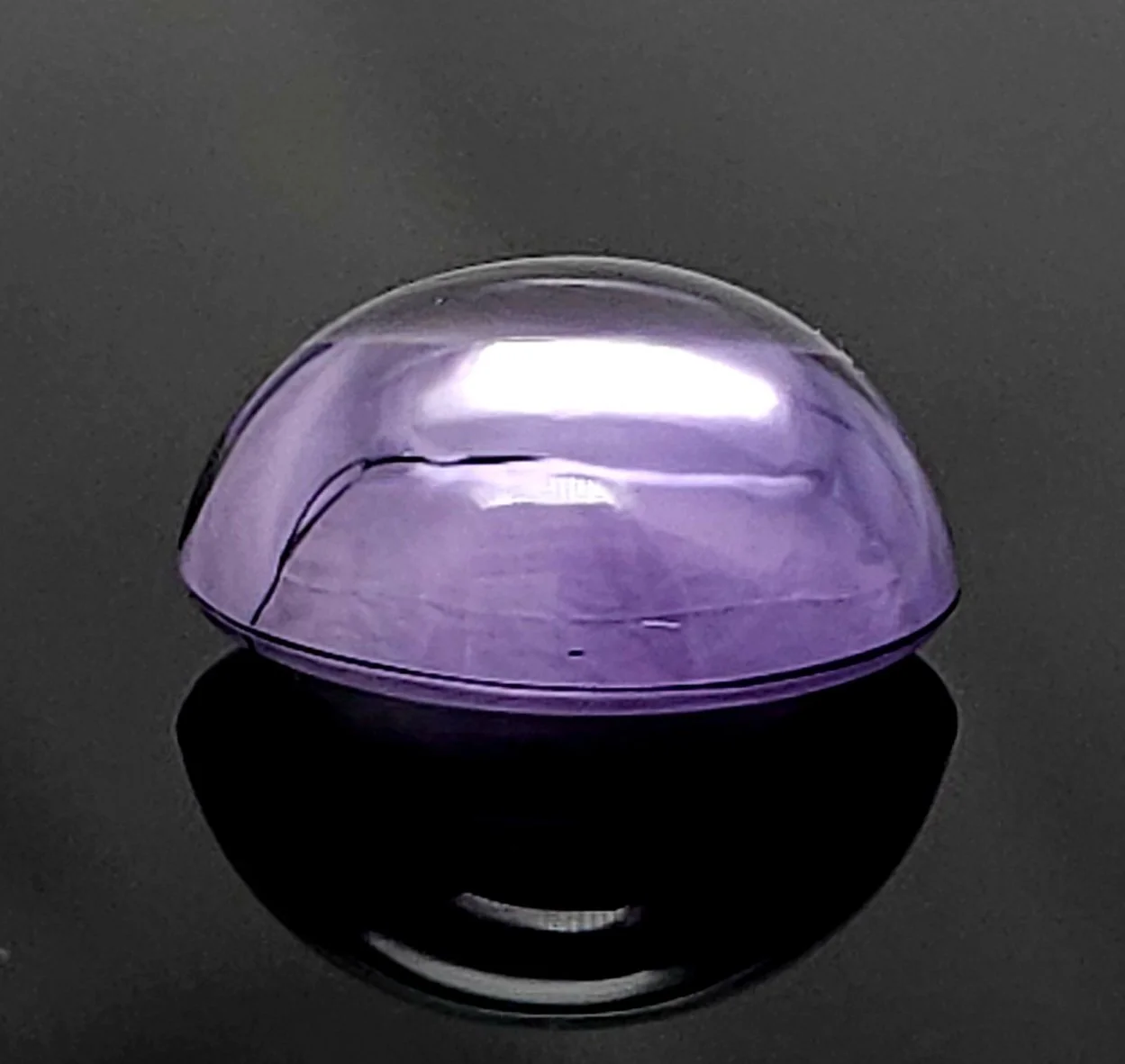 Amethyst cabochon resting on a grey reflective surface.