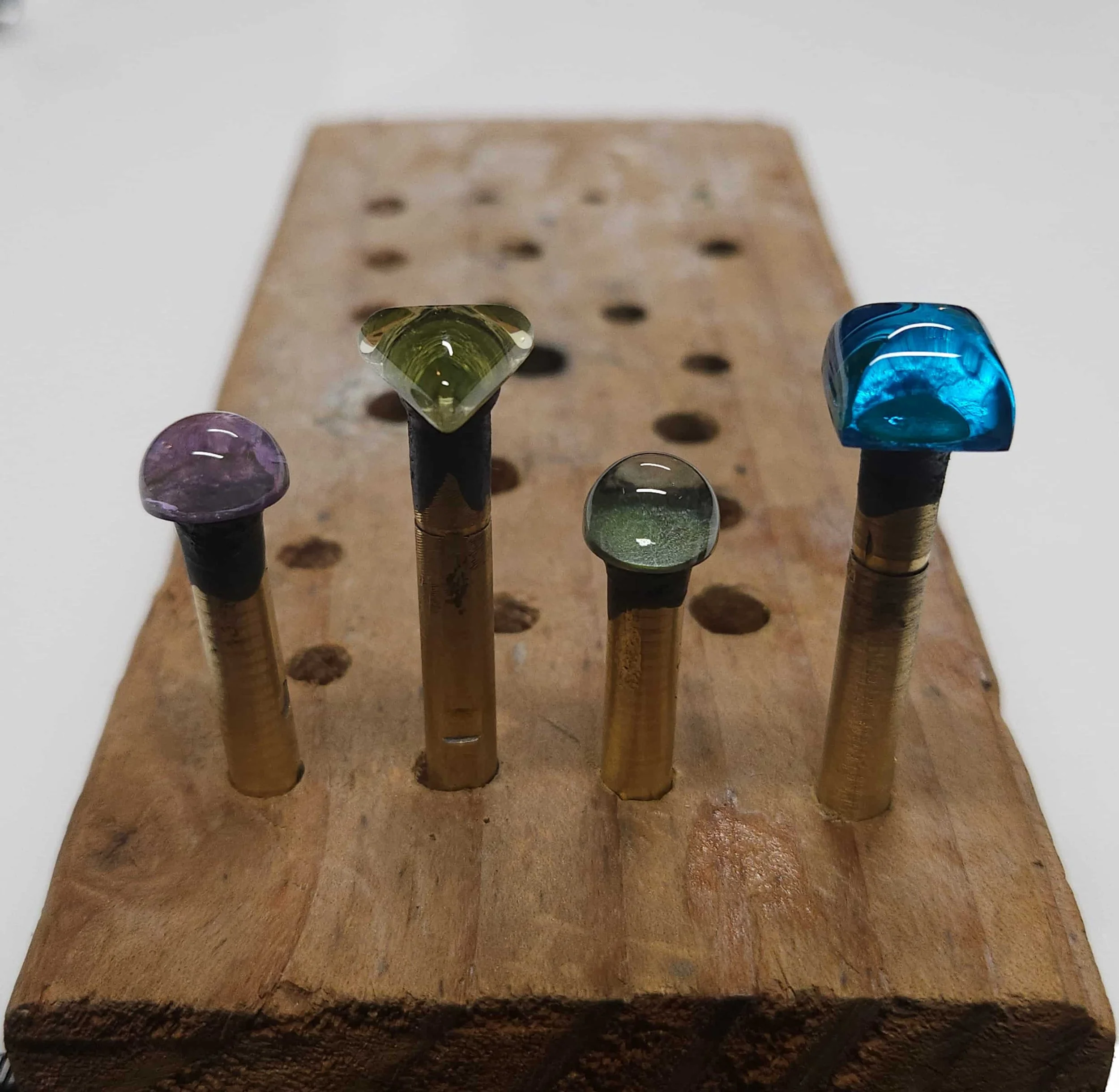 Close-up of five colorful quartz cabochons placed on a wooden surface with holes, with a blurred wooden block in the background.