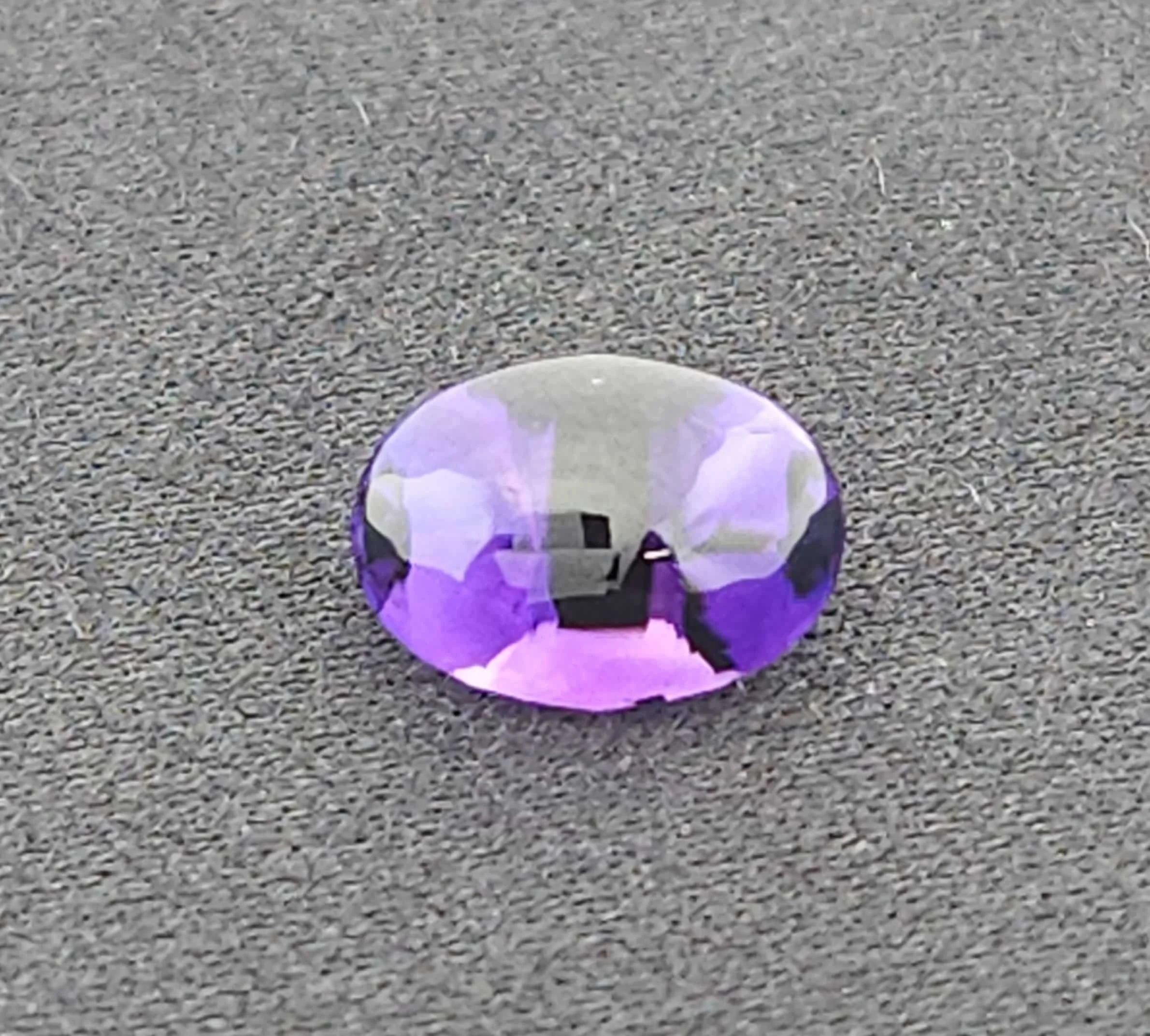 A small, purple and white dinosaur figurine or toy on a gravel surface.