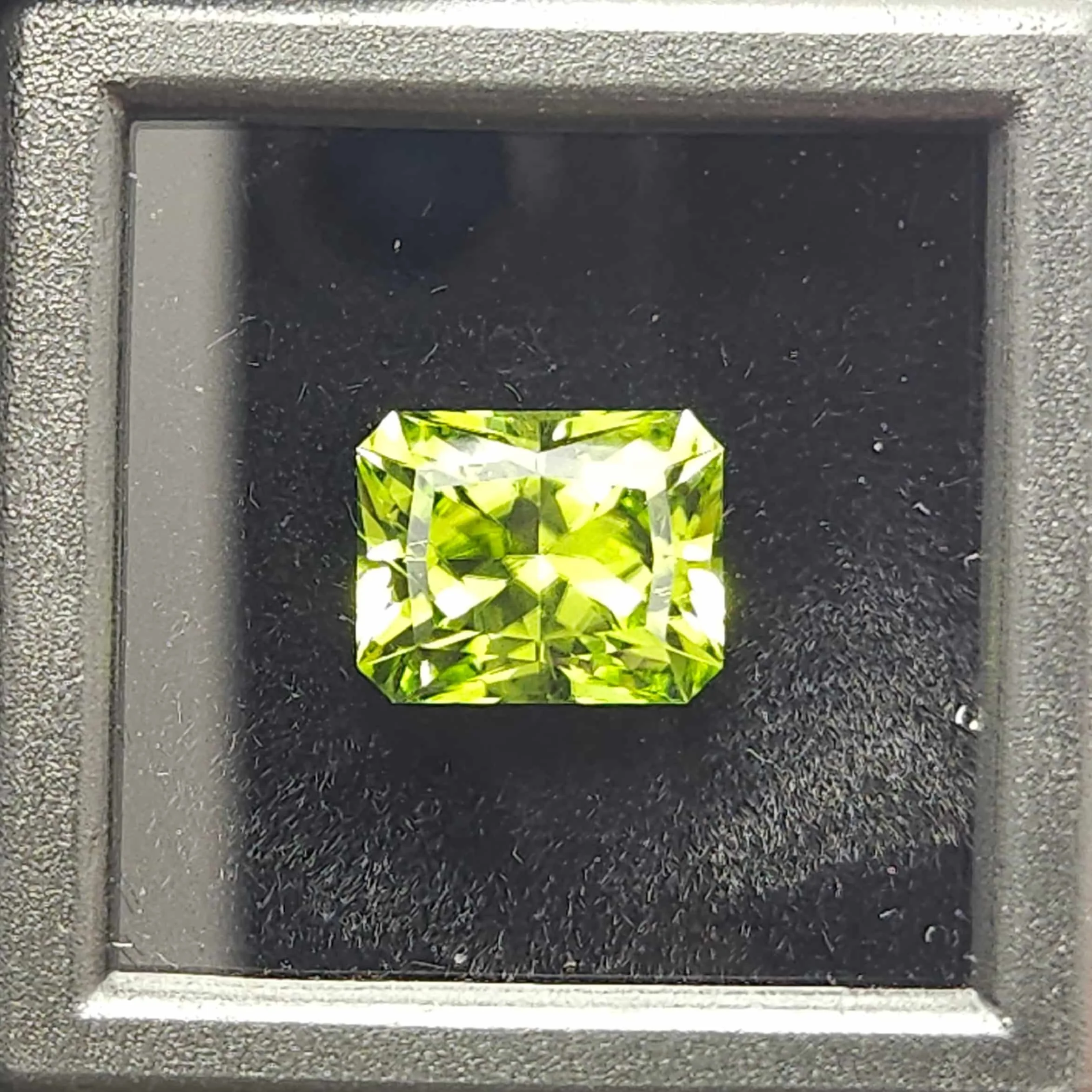 close up of a finished peridot gemstone in a black display box.