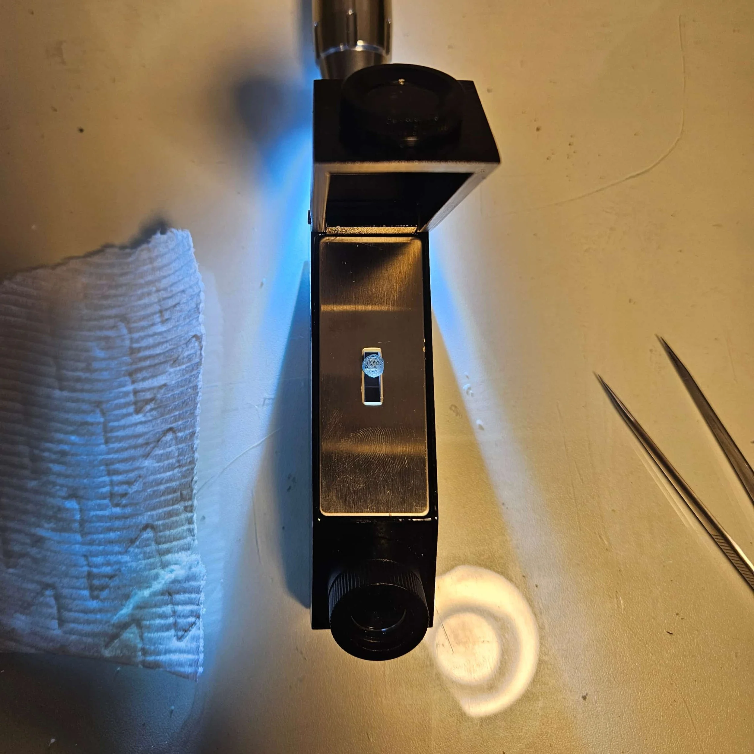 A open refractometer with a sapphire on it with a light from the back resting on a counter top.