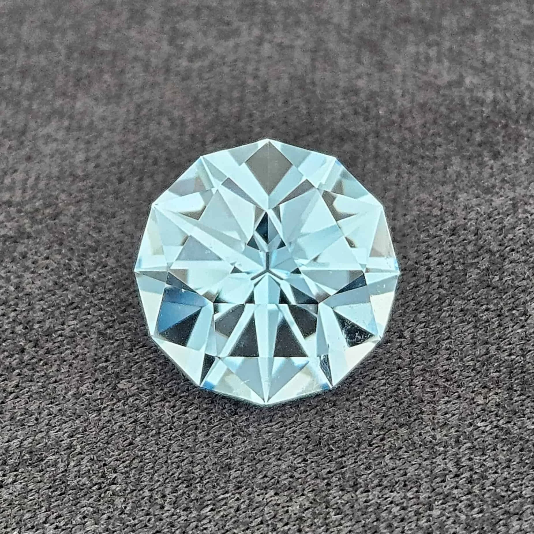 A faceted, clear, diamond-shaped crystal ornament placed on a dark, textured surface.