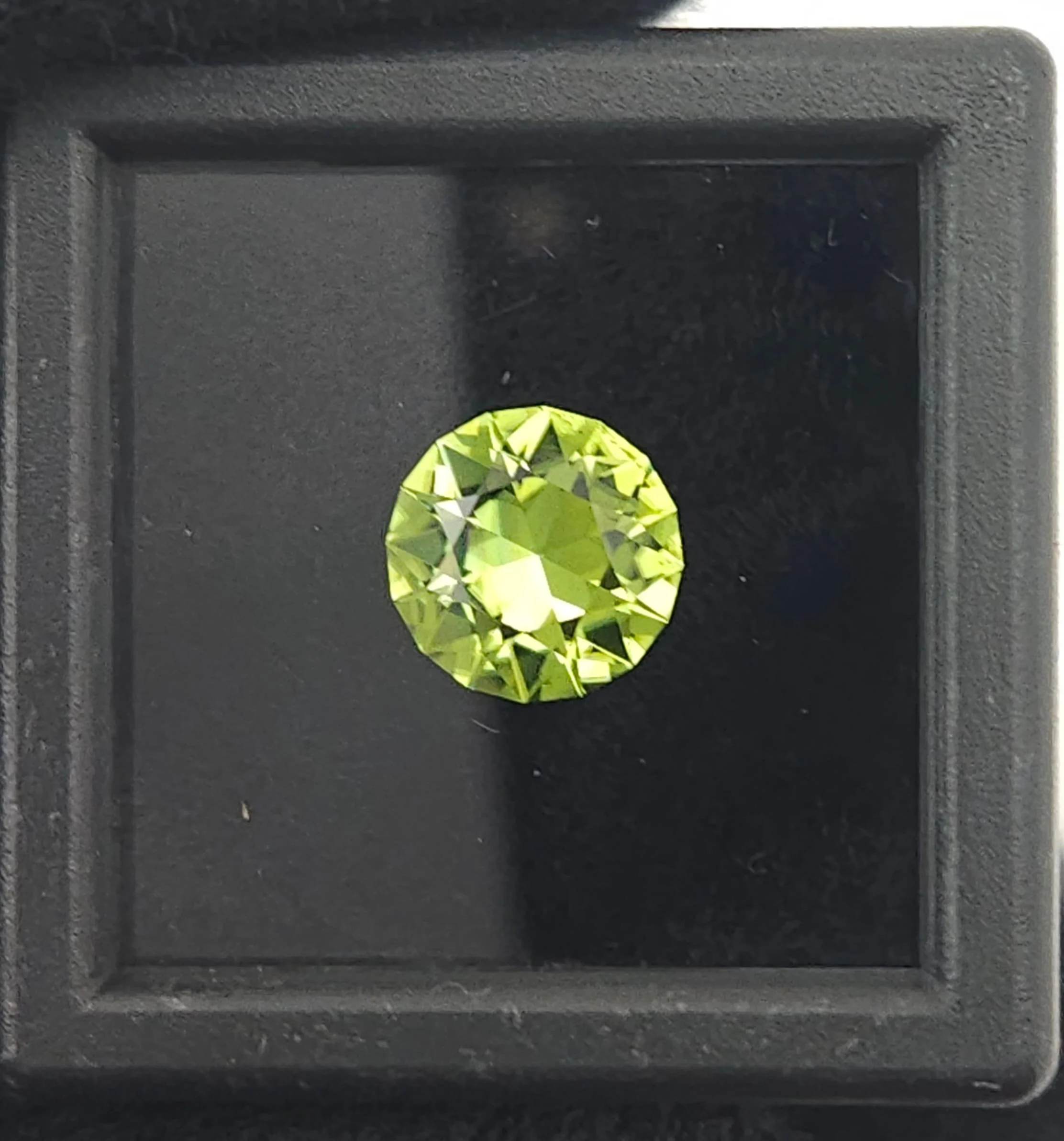 Peridot gemstone in a black glass top gem case.