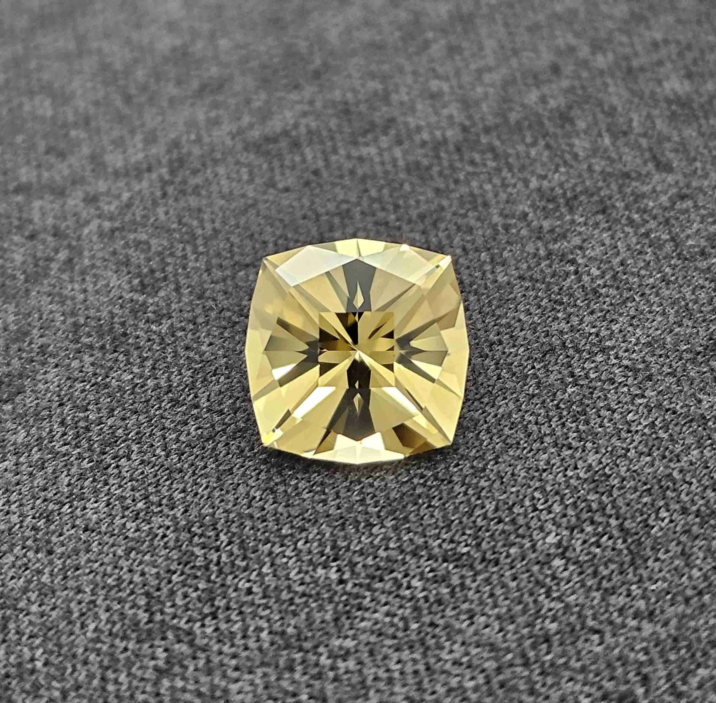 A faceted golden gemstone on a gray, textured surface.