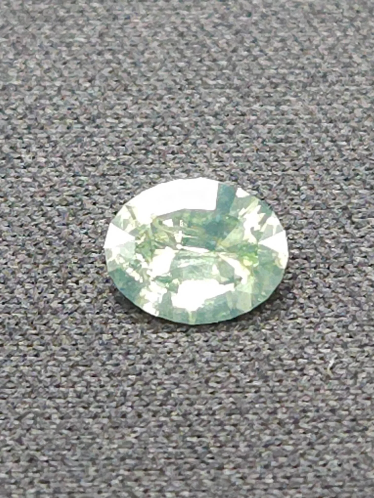 a precision faceted green Montana sapphire resting on a grey surface.