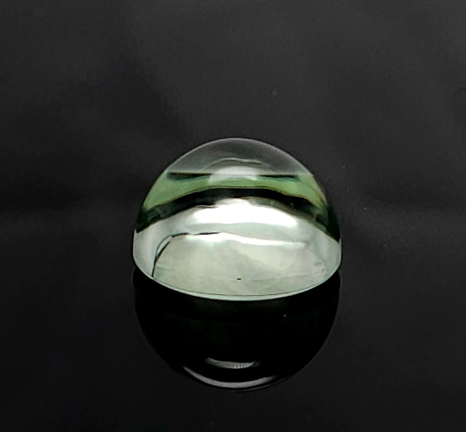 Prasiolite round cabochon resting on a black reflective surface