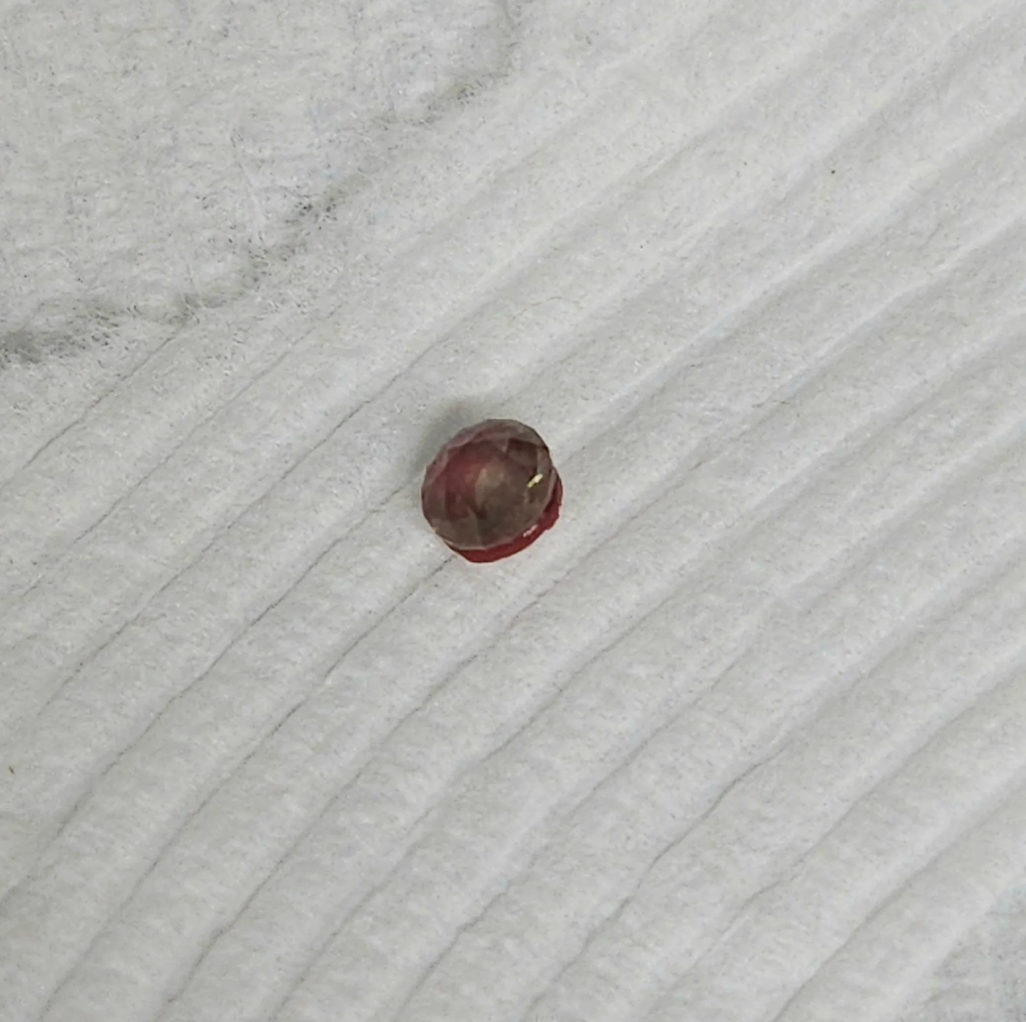 A sapphire that has been faceted with wax still on it resting on a white textured surface.