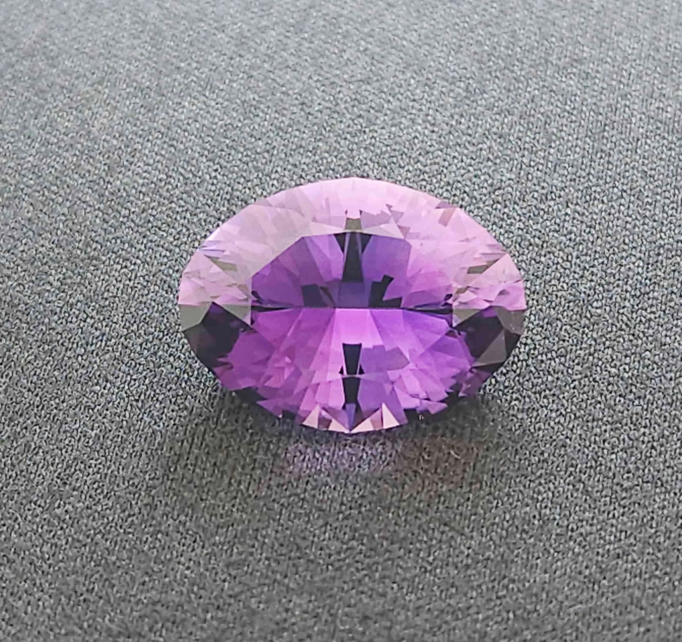 precision cut amethyst oval resting on a grey cloth