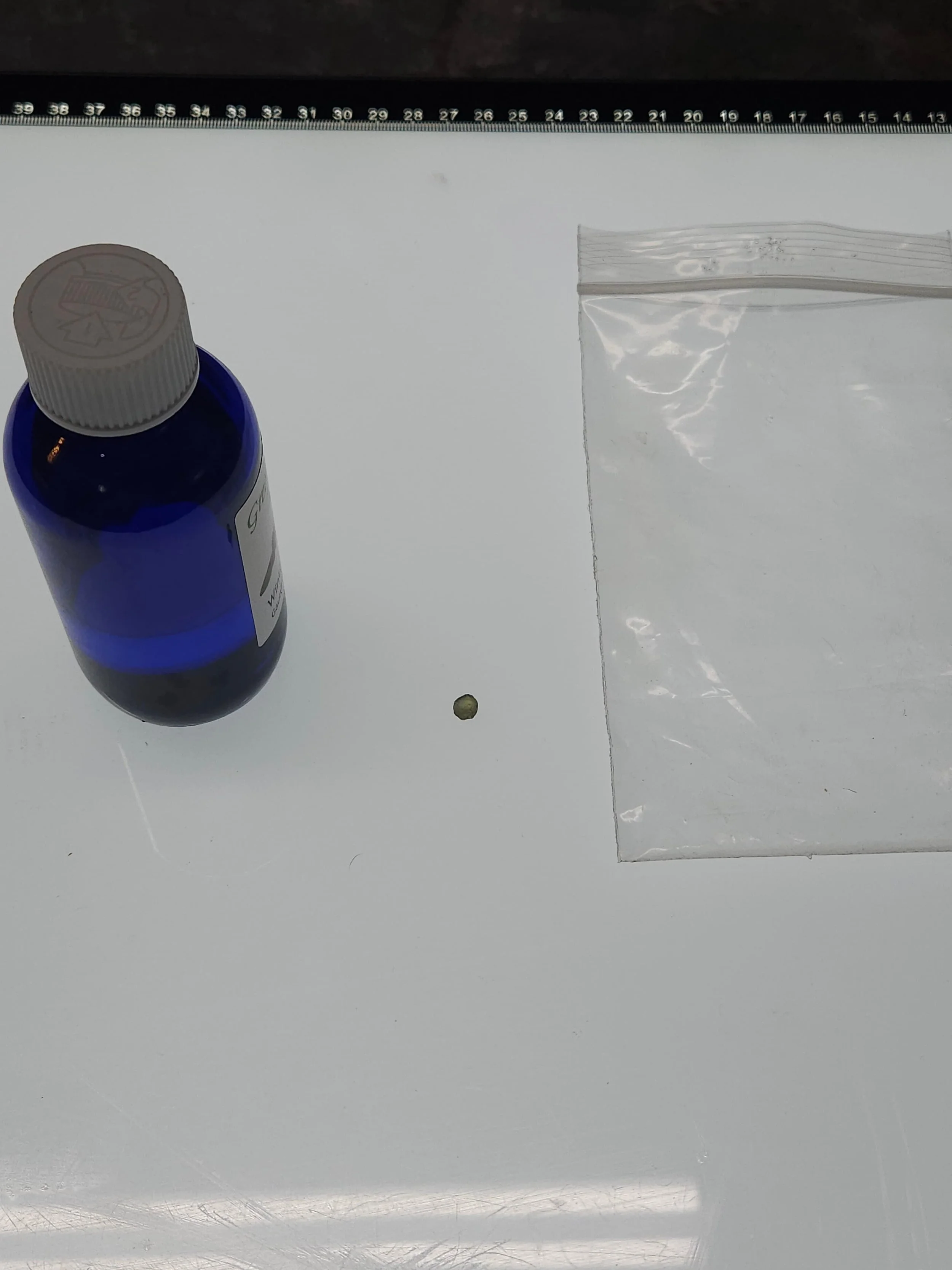 A bottle of oil, a Montana Sapphire, and a clear bag resting on a light table.