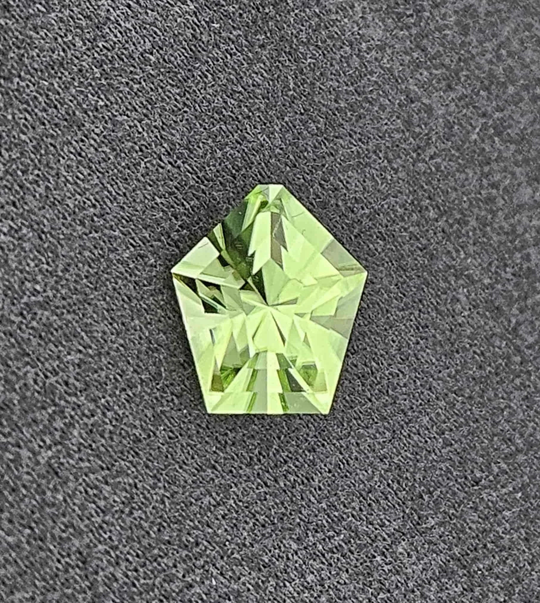 A small green paper origami frog on a dark gray textured carpet.