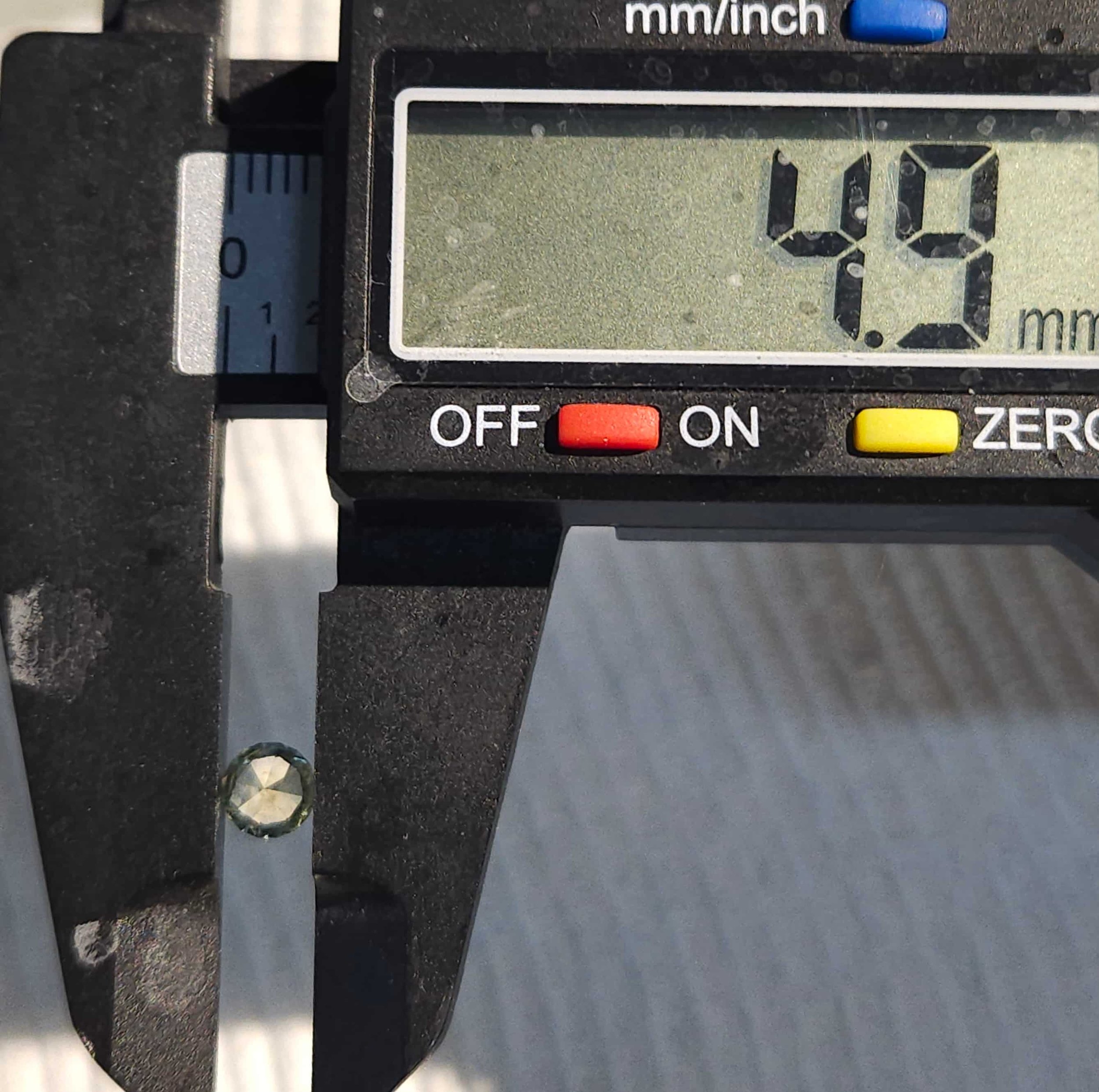Close-up of a digital caliper measuring a small,yellow/green, faceted sapphire.