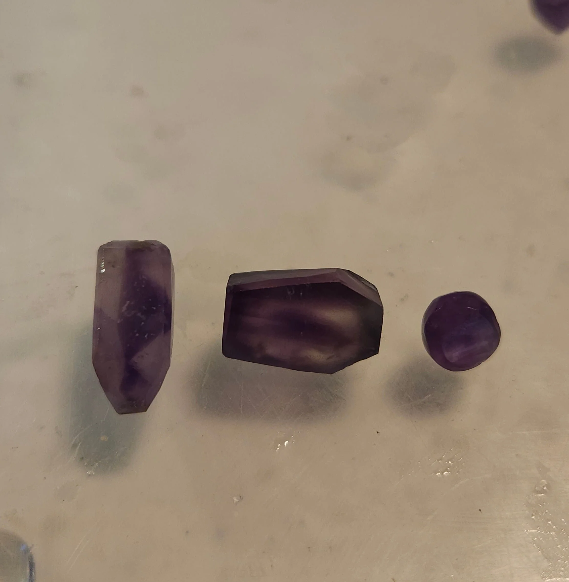 A close-up of a couple of purple crystals with a shiny, glossy surface, resting on a reflective surface.