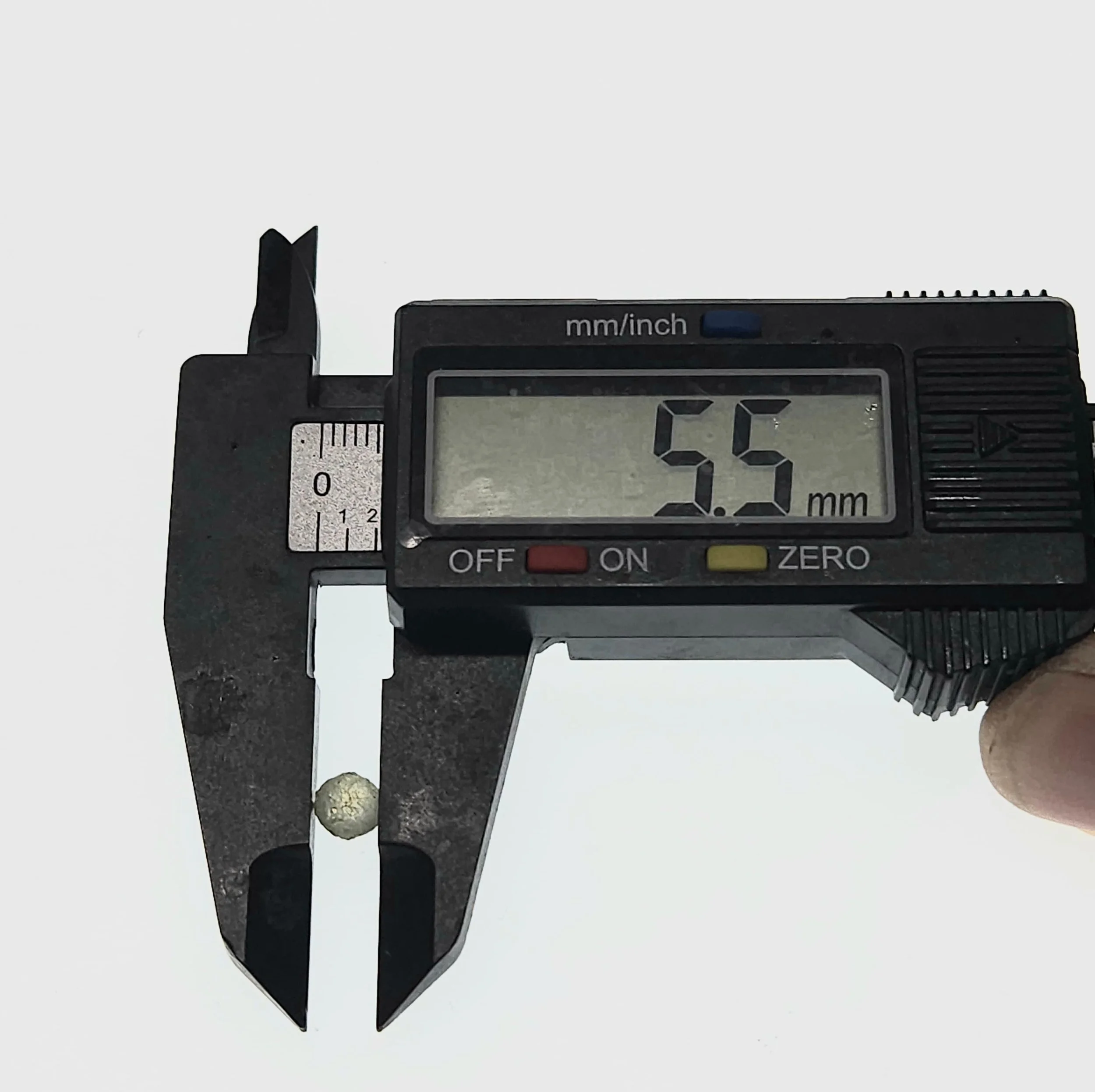 A digital caliper measuring the diameter of a rough Montana Sapphire, displaying a reading of 5.5 mm.