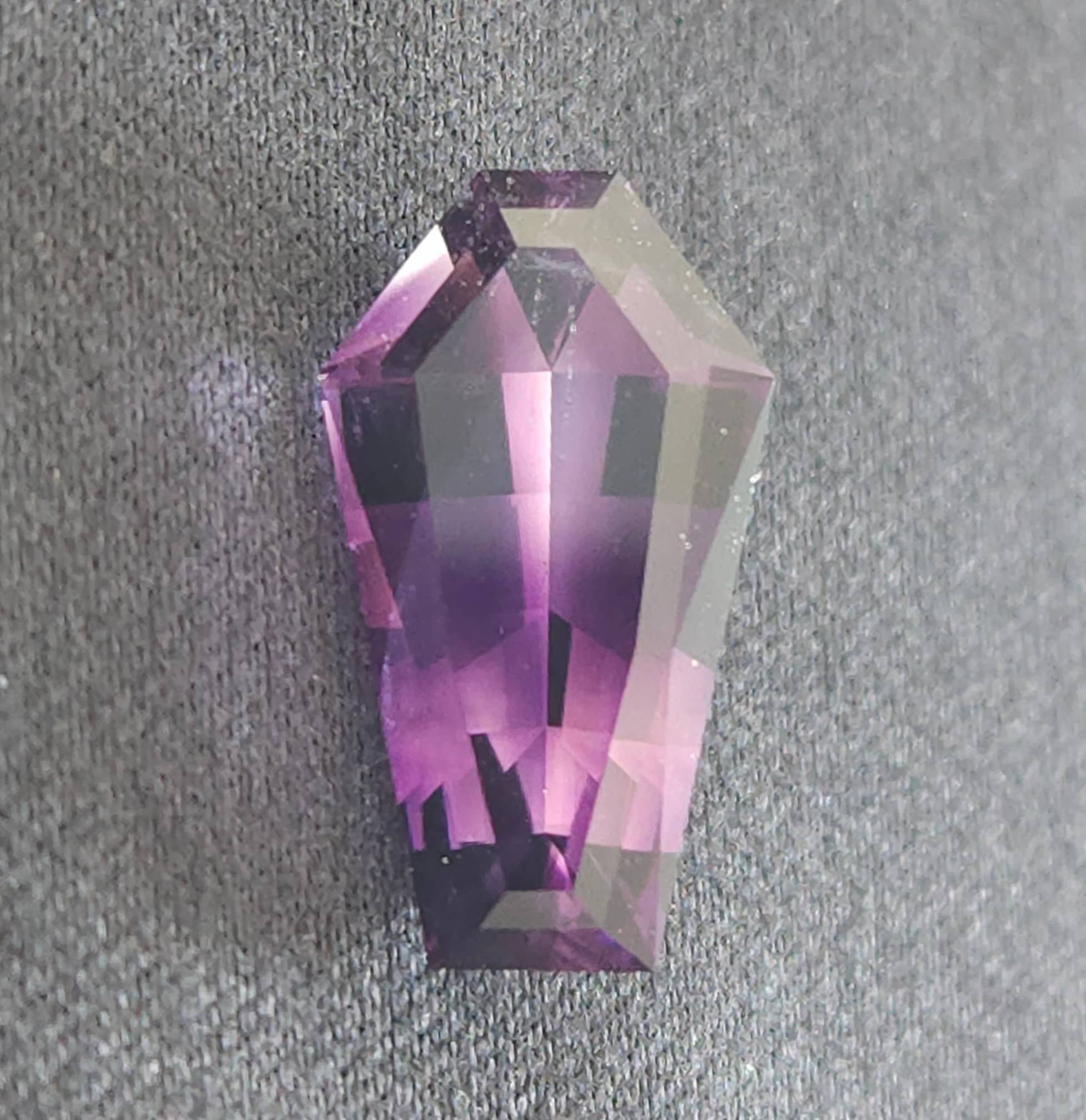 Close-up of a purple, faceted gemstone on a textured gray surface.