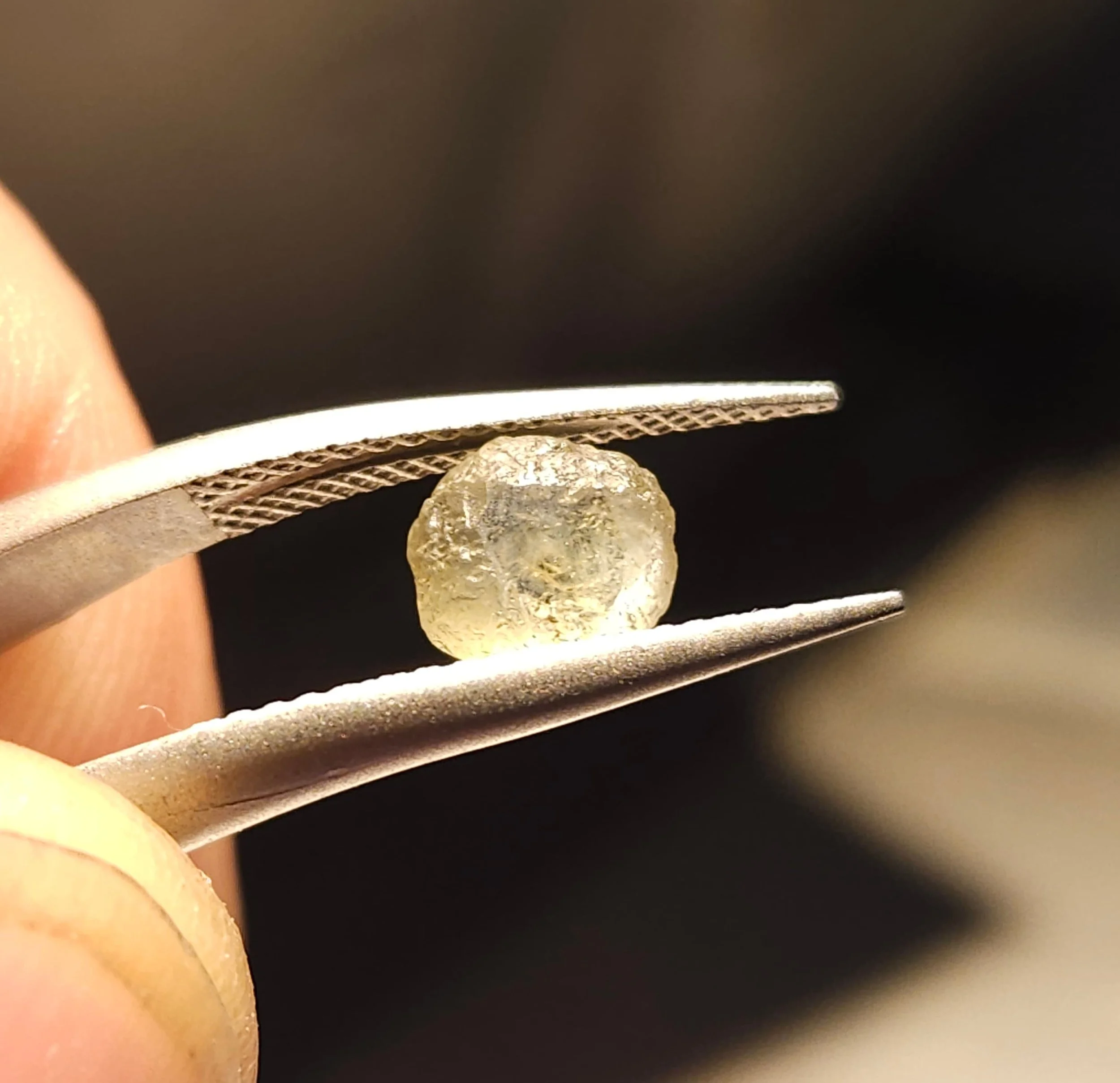 Close-up of a sapphire held with tweezers, with a blurred background.