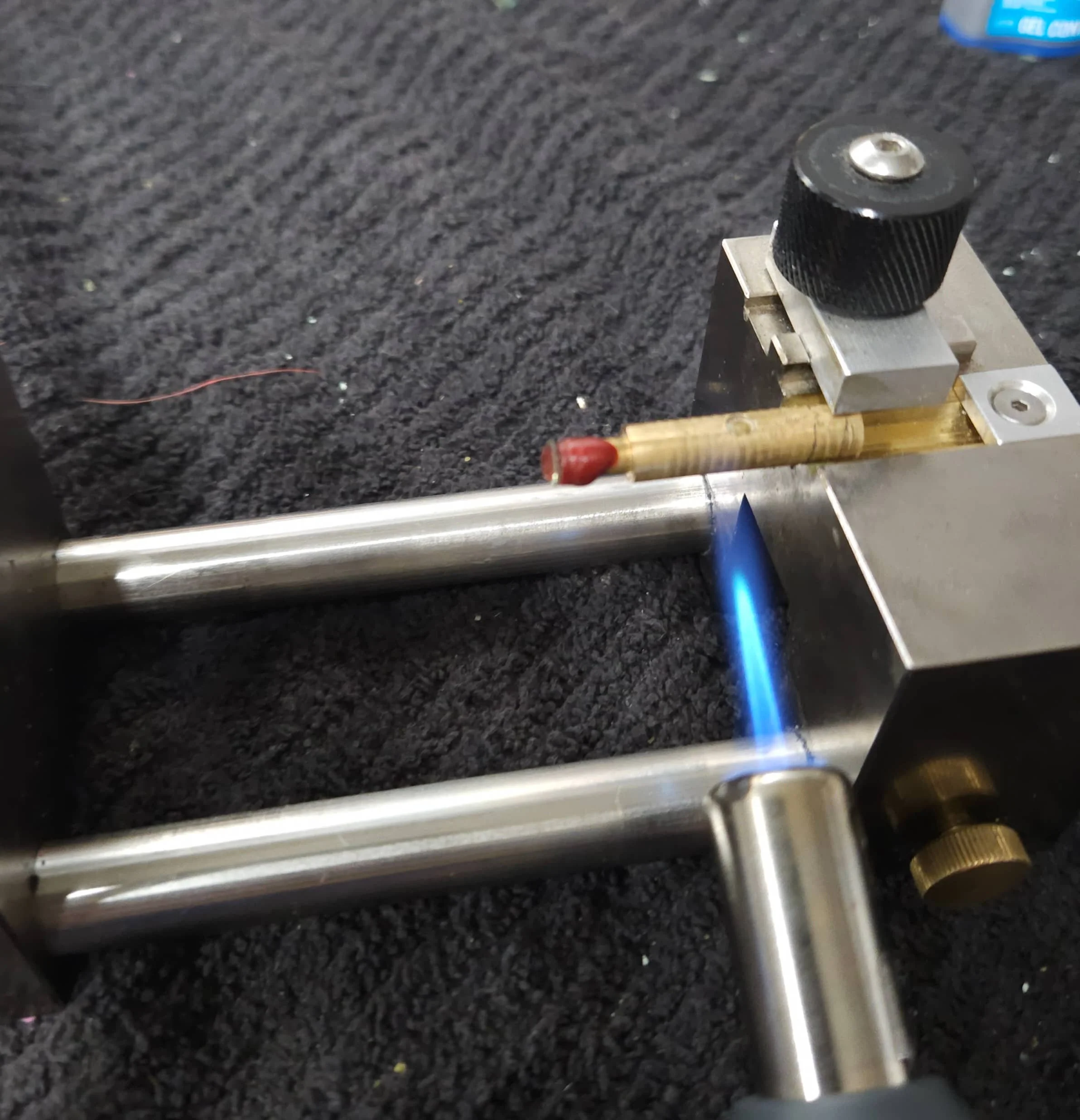 Close-up of a sapphire being removed from a brass dop with a blue lighter flame below, on a black textured surface.