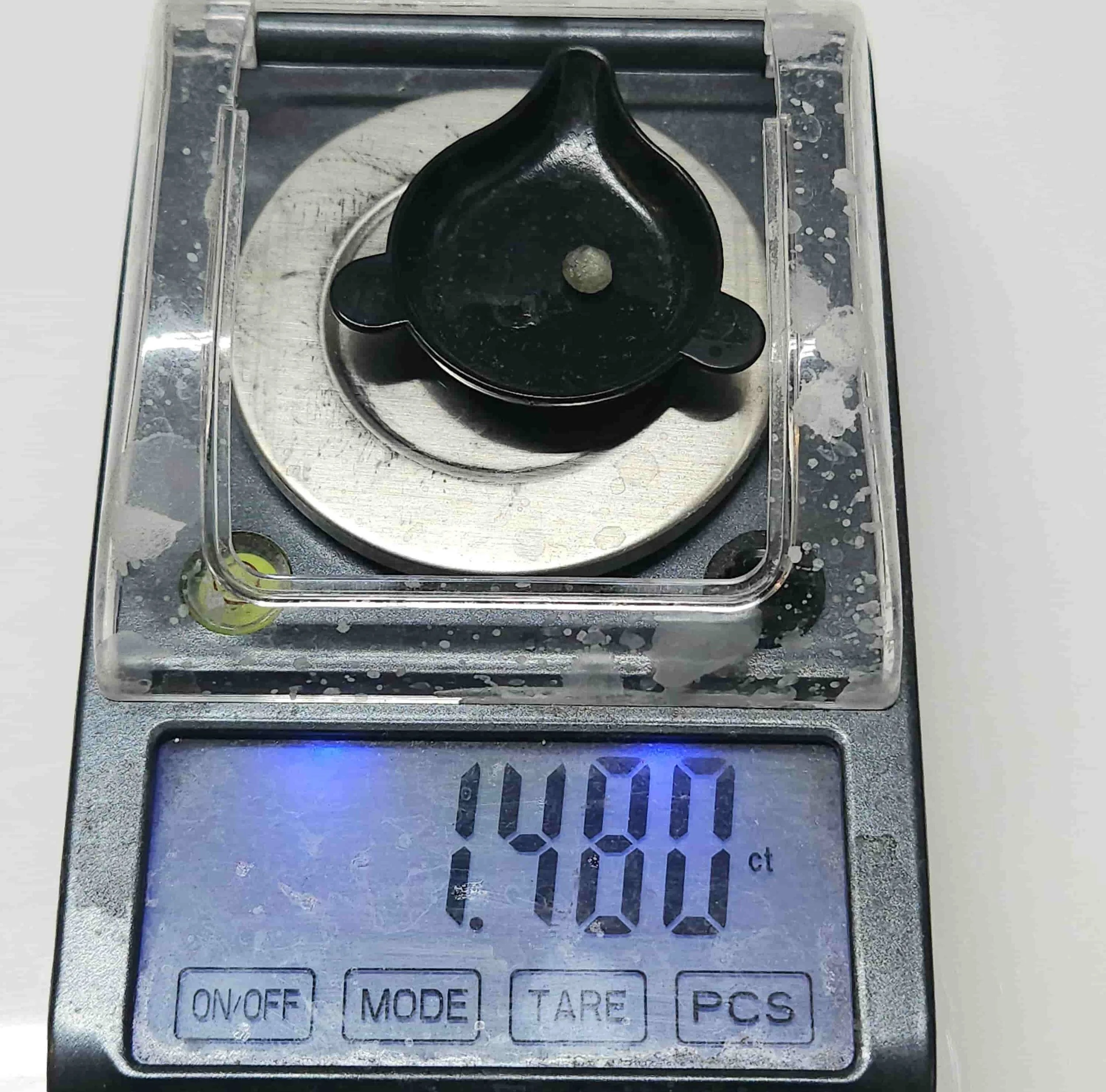 Close-up of a well worn lab scale measuring the weight of a rough Montana Sapphire at 1.48ct.
